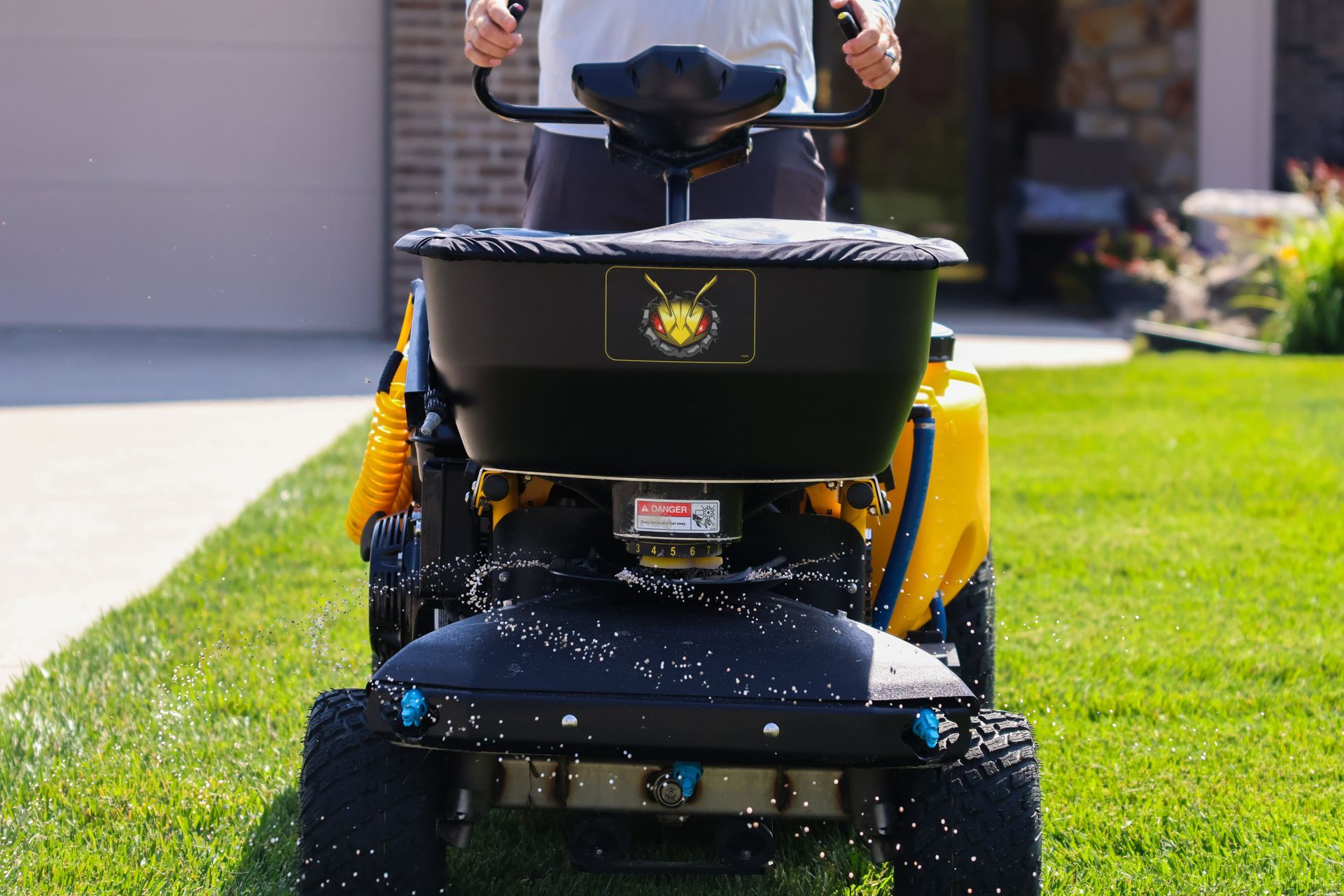 Person driving a yellow spreader on a lawn, dispensing white granules.