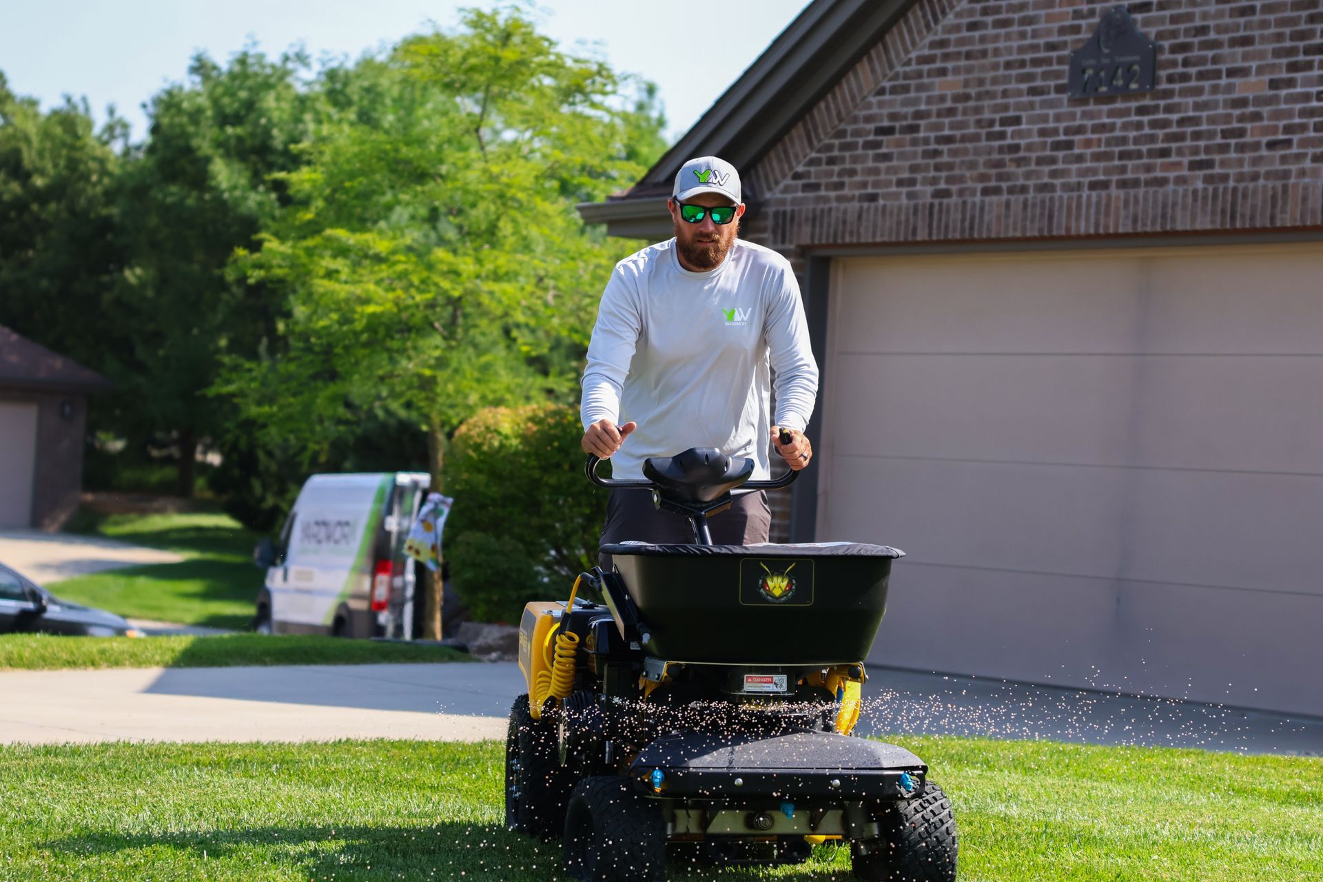 Man operating a fertilizer spreader on a lawn, next to a garage and a truck.