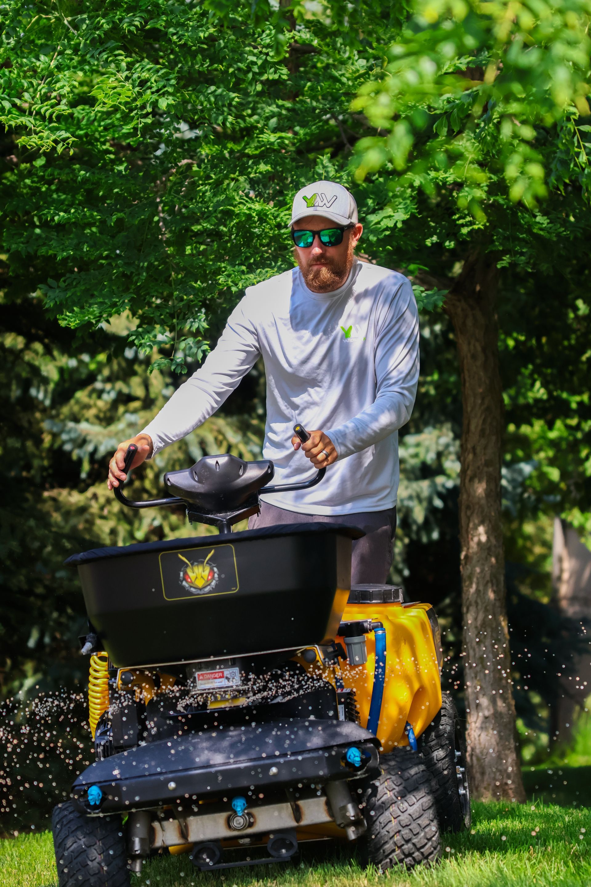 Man operating a yellow lawn spreader, applying granular product to a green lawn.