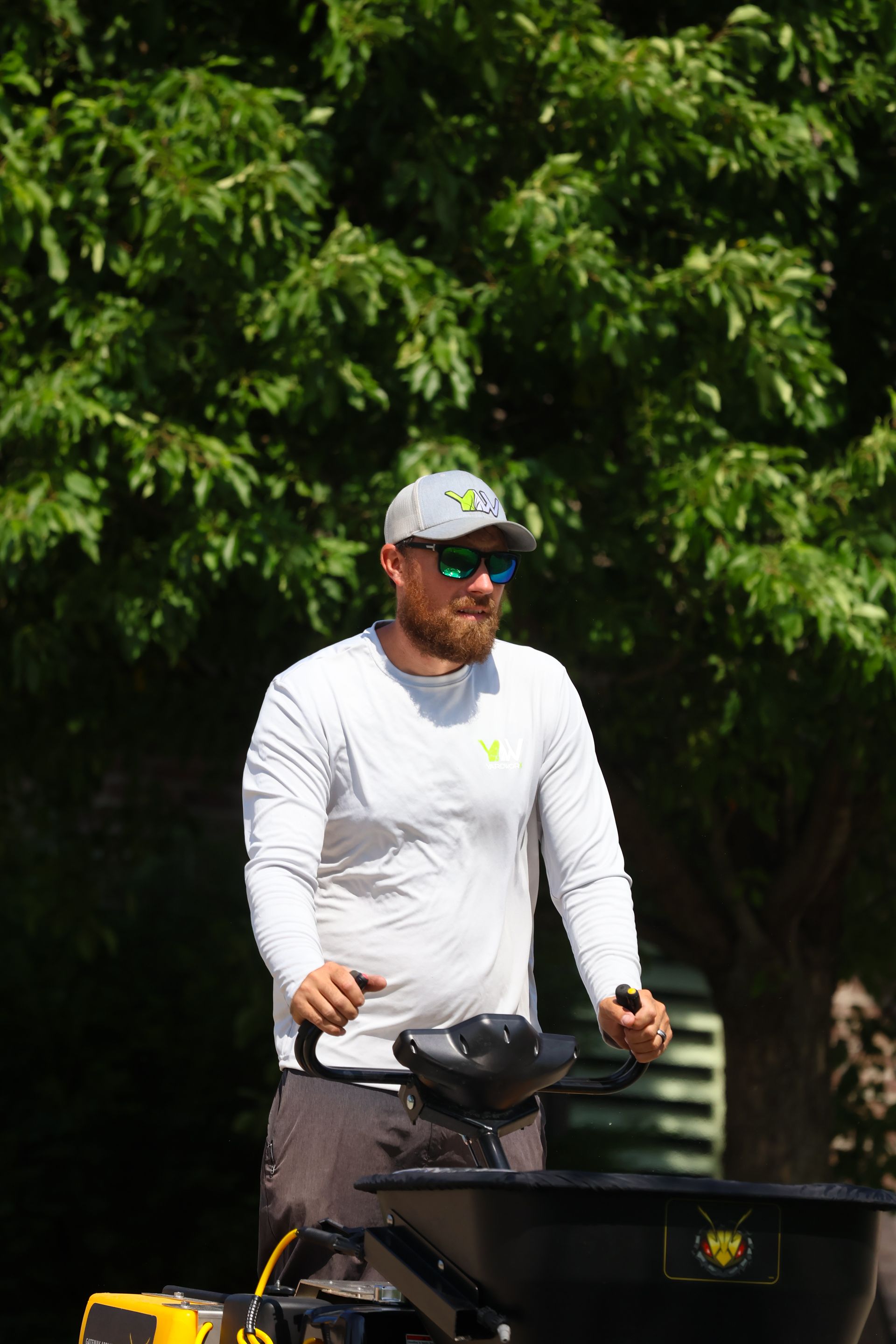 Man in sunglasses operating a machine, outdoors near trees.