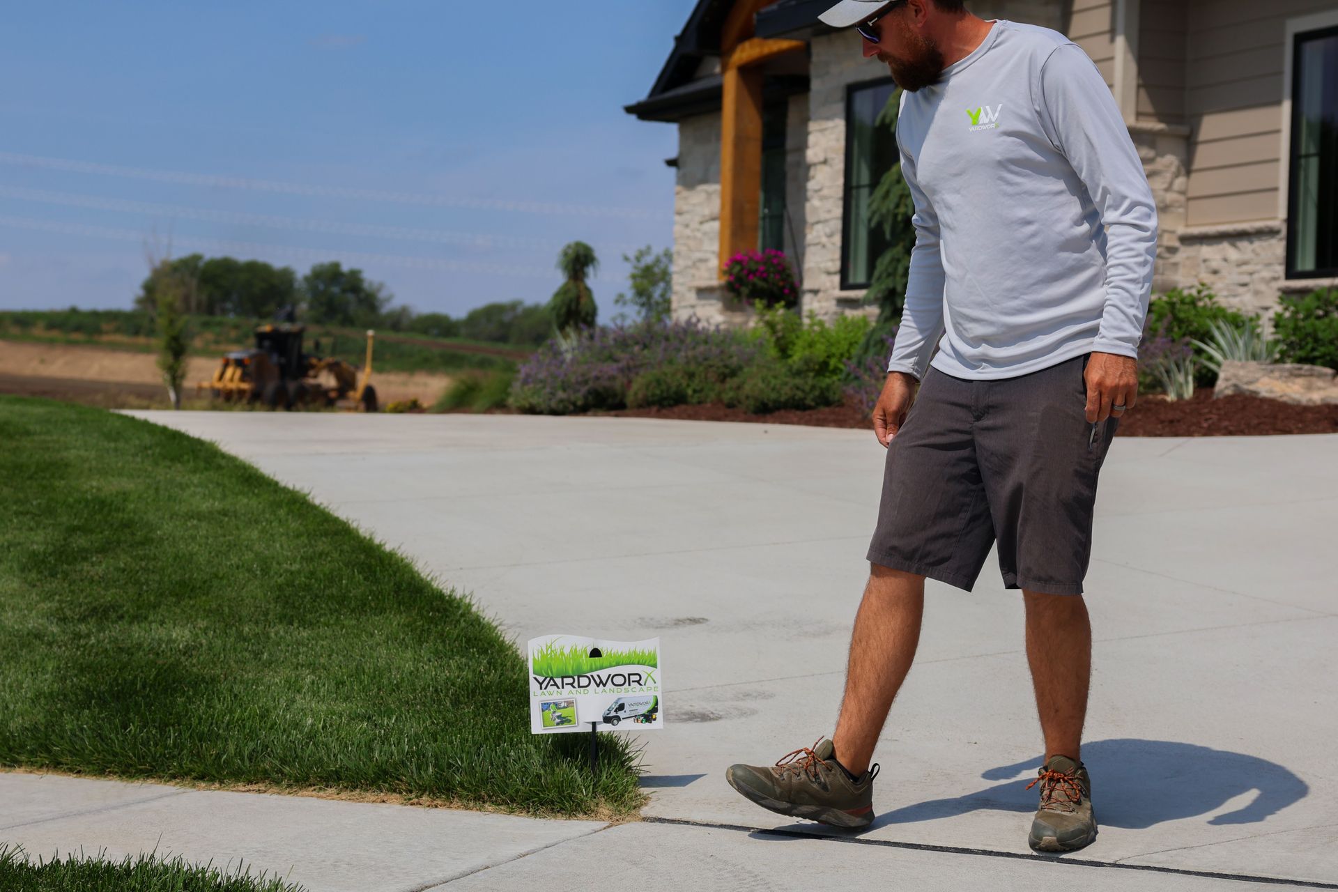 Man near sign on sidewalk next to grass and house.