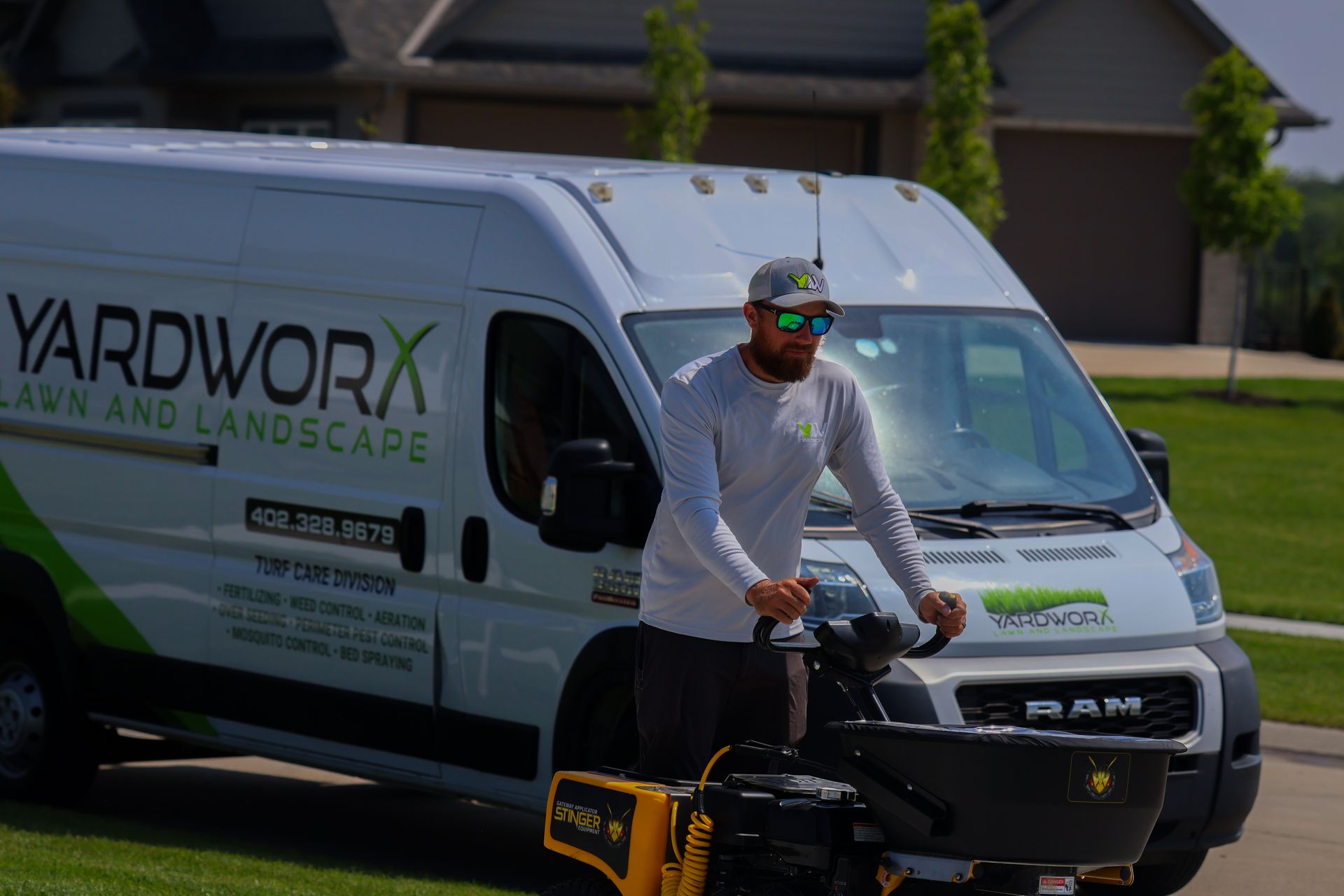 Man operating a lawn spreader in front of a Yardworx van; sunny day.