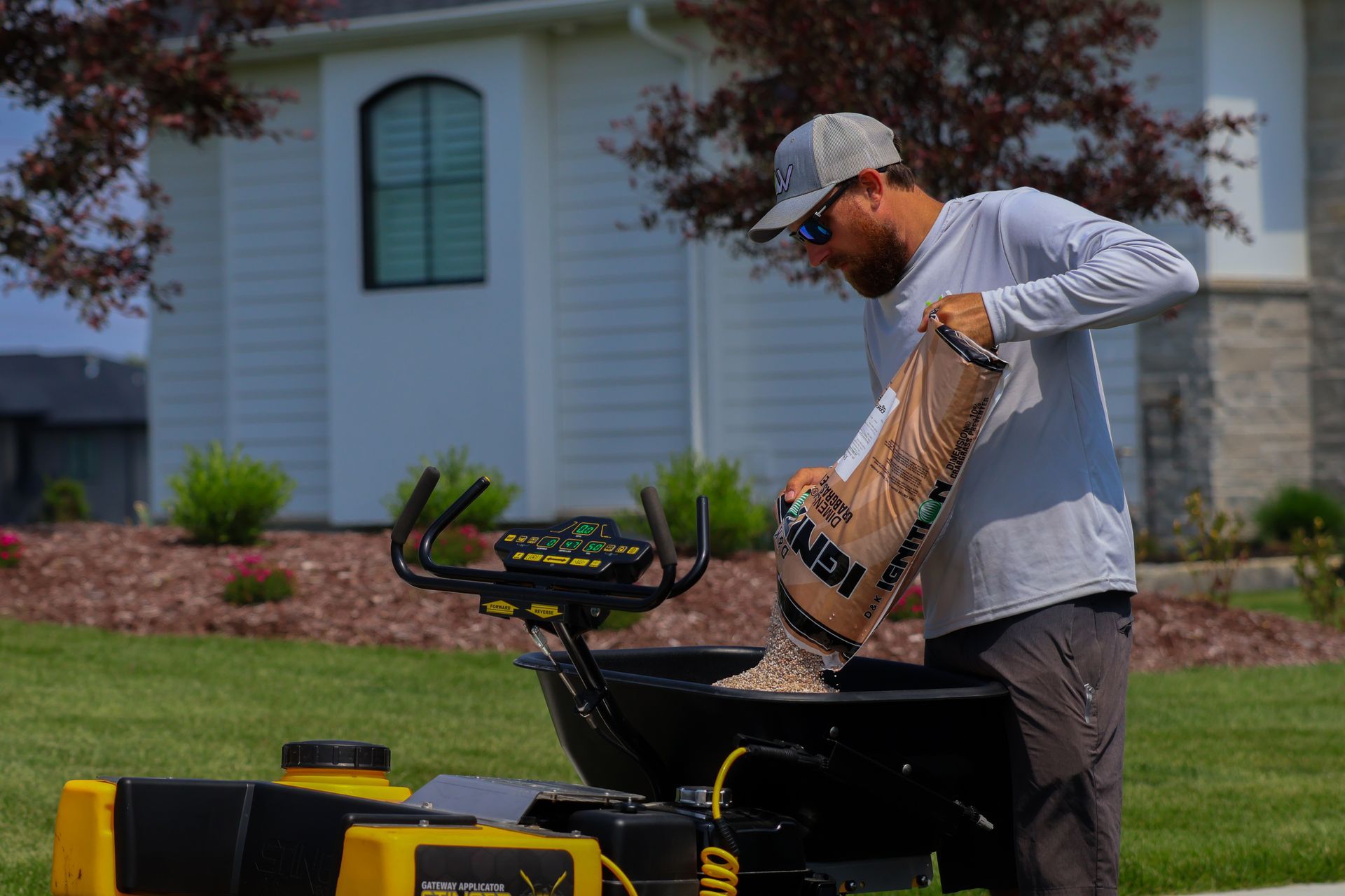 Man pouring material from a bag into a lawn spreader on a grassy lawn.