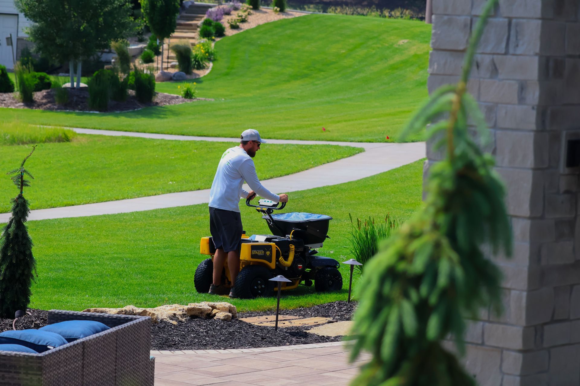 Man using a spreader on a lawn, rolling on a yellow machine. Green grass, pathway, and building in the background.