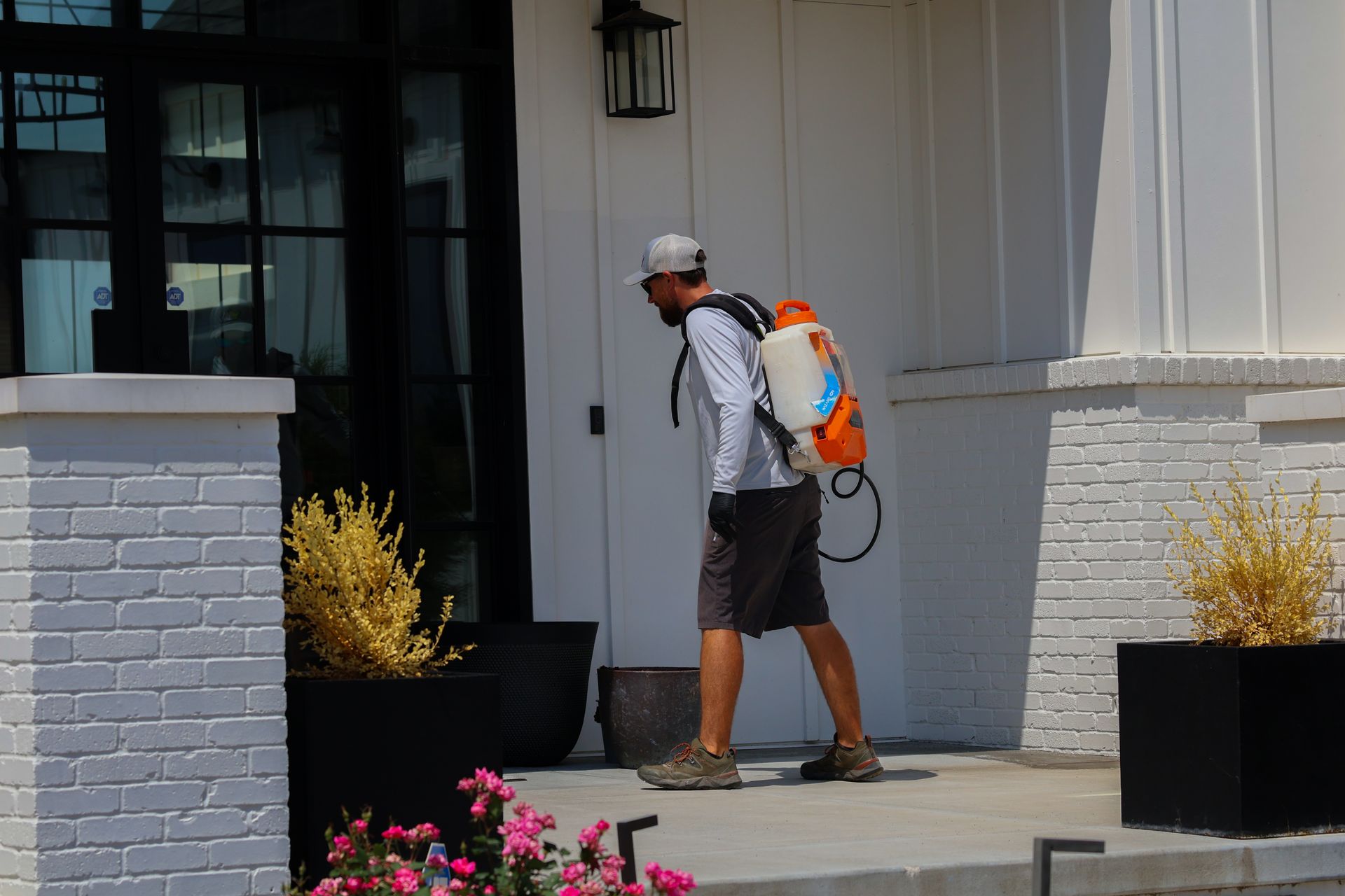 Man with sprayer on his back near a house, possibly pest control.