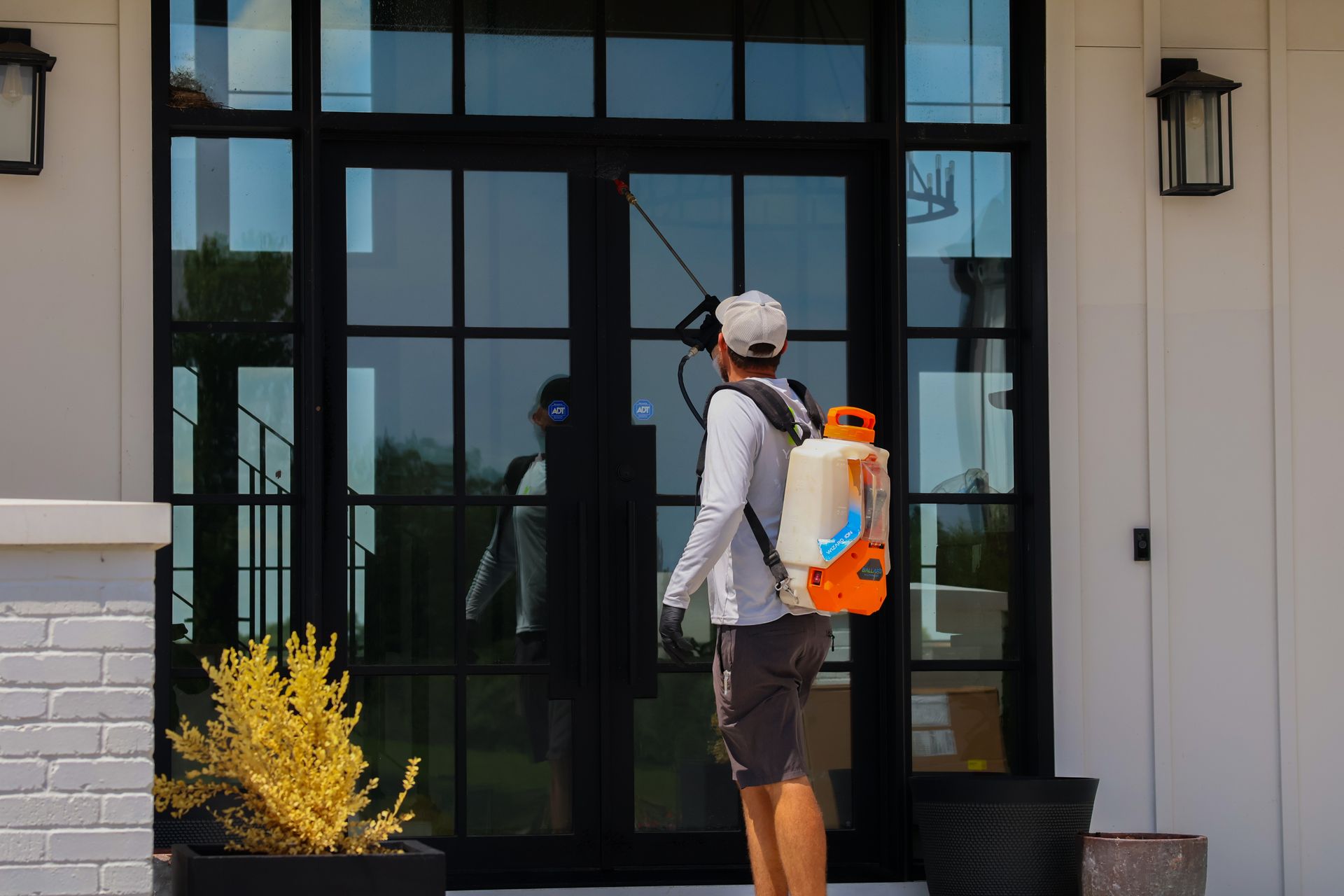 Person spraying a front door with a backpack sprayer, exterior of a modern house.