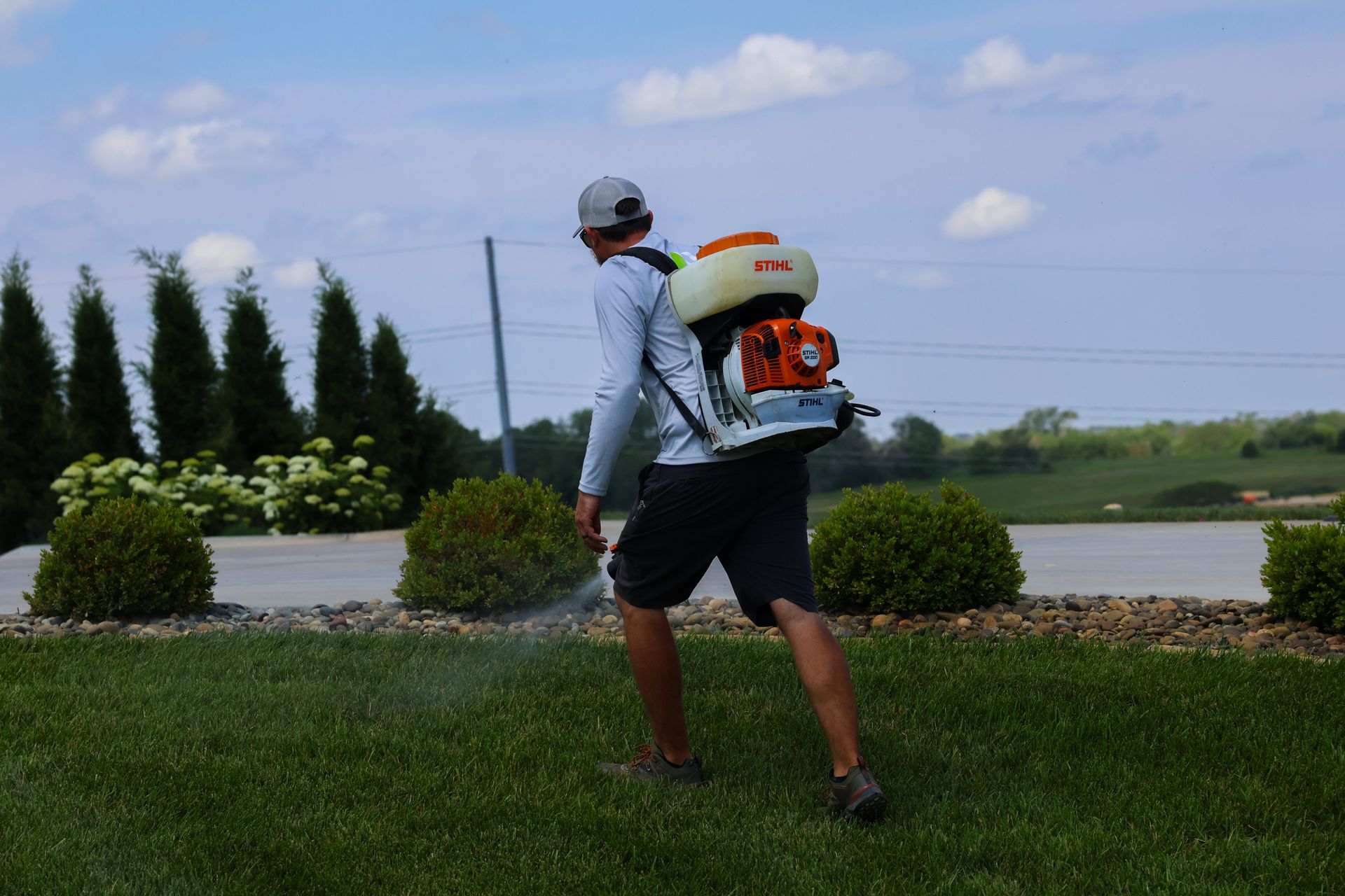 Person spraying lawn with a backpack sprayer outdoors.