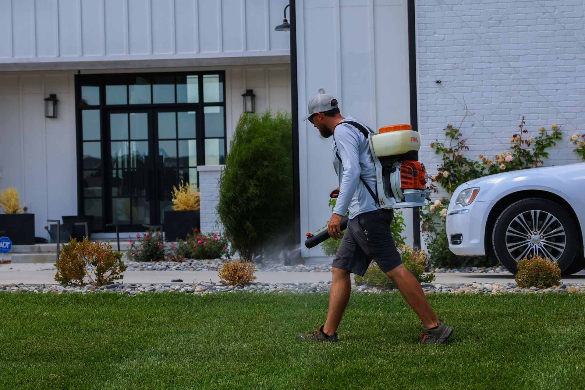 Man spraying a lawn with a backpack sprayer in front of a house.