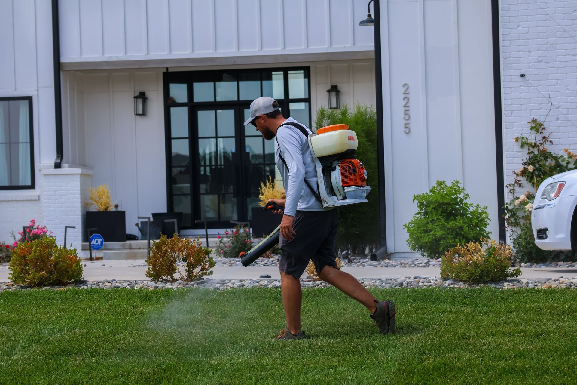 Man using a leaf blower on a lawn in front of a house.