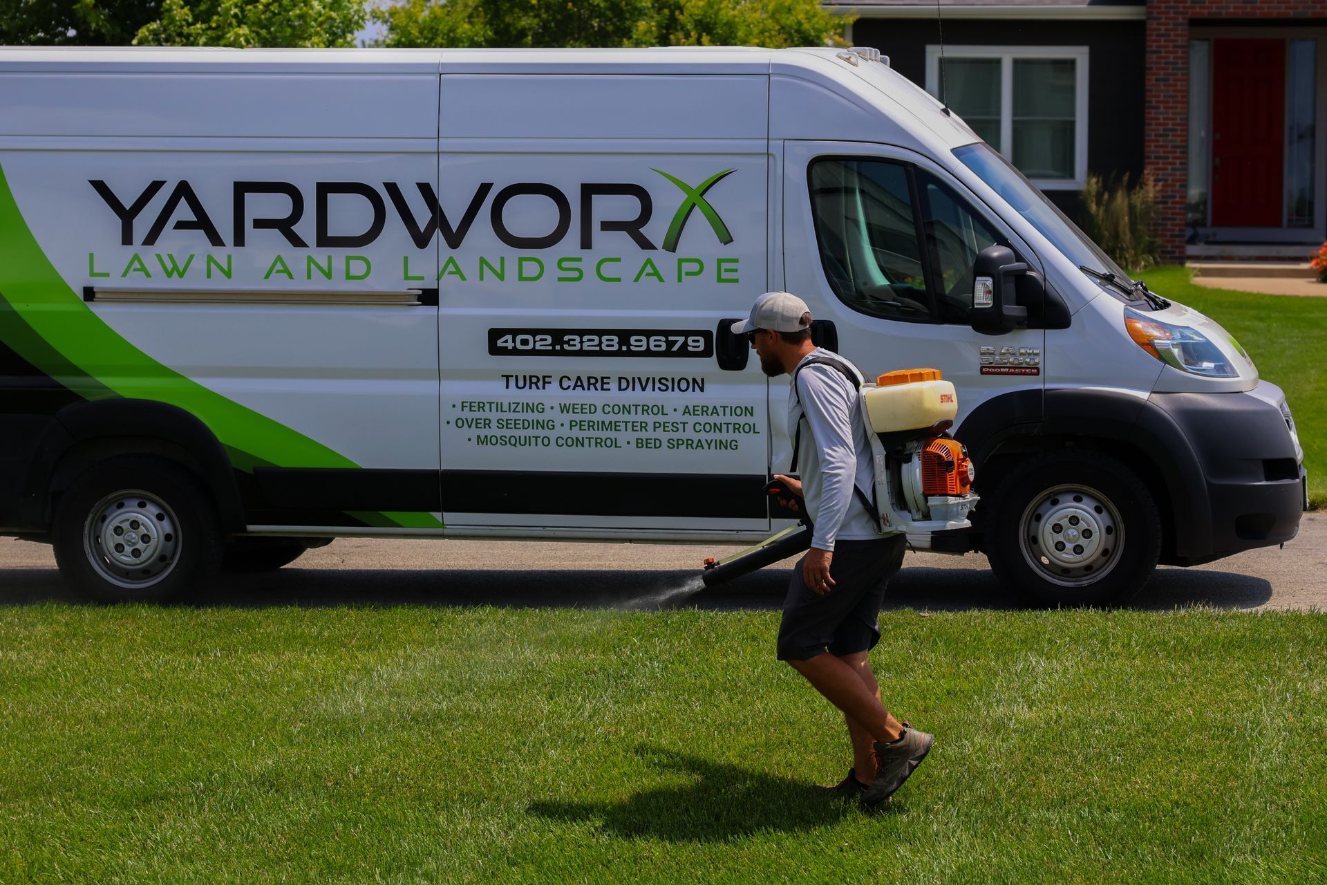 Man using a leaf blower on green lawn next to a white Yardworx van.