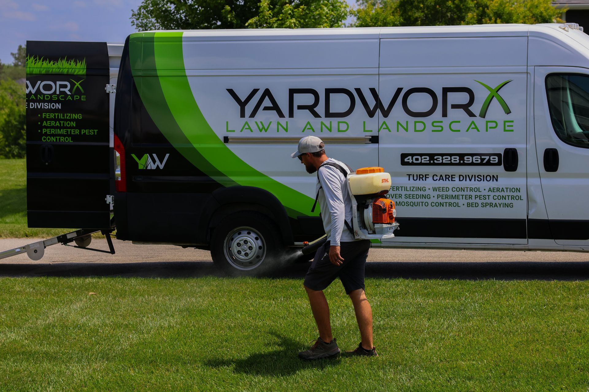 Man spraying lawn with backpack sprayer near a van labeled 