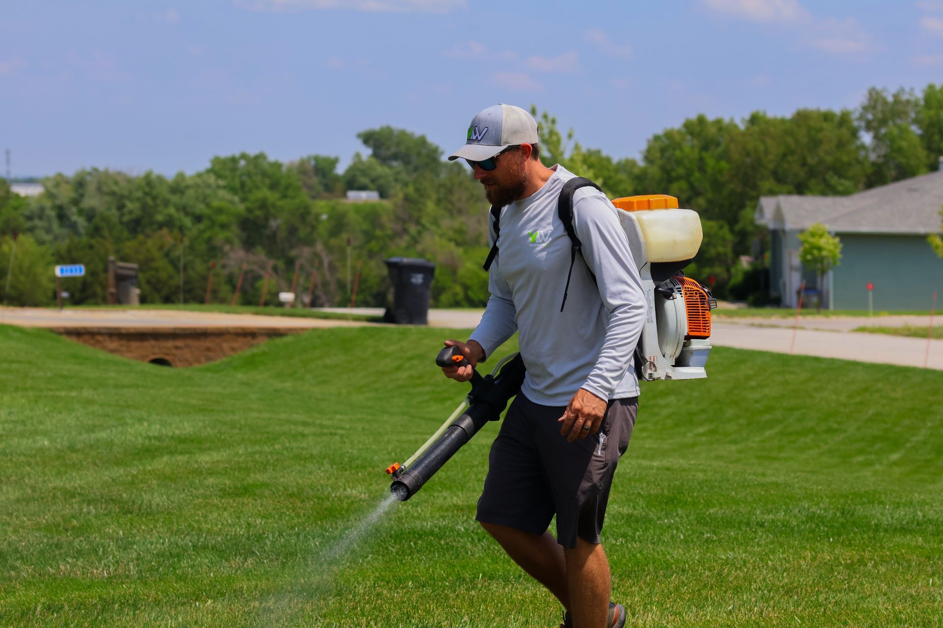 Man spraying liquid from a backpack sprayer onto grass in a yard.