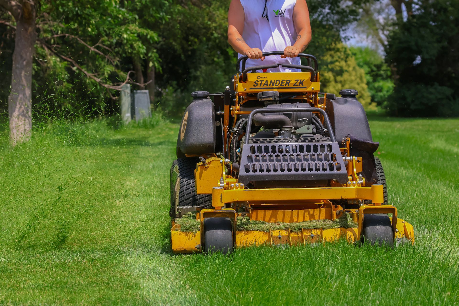 Man mowing lawn with yellow zero-turn mower on a sunny day.