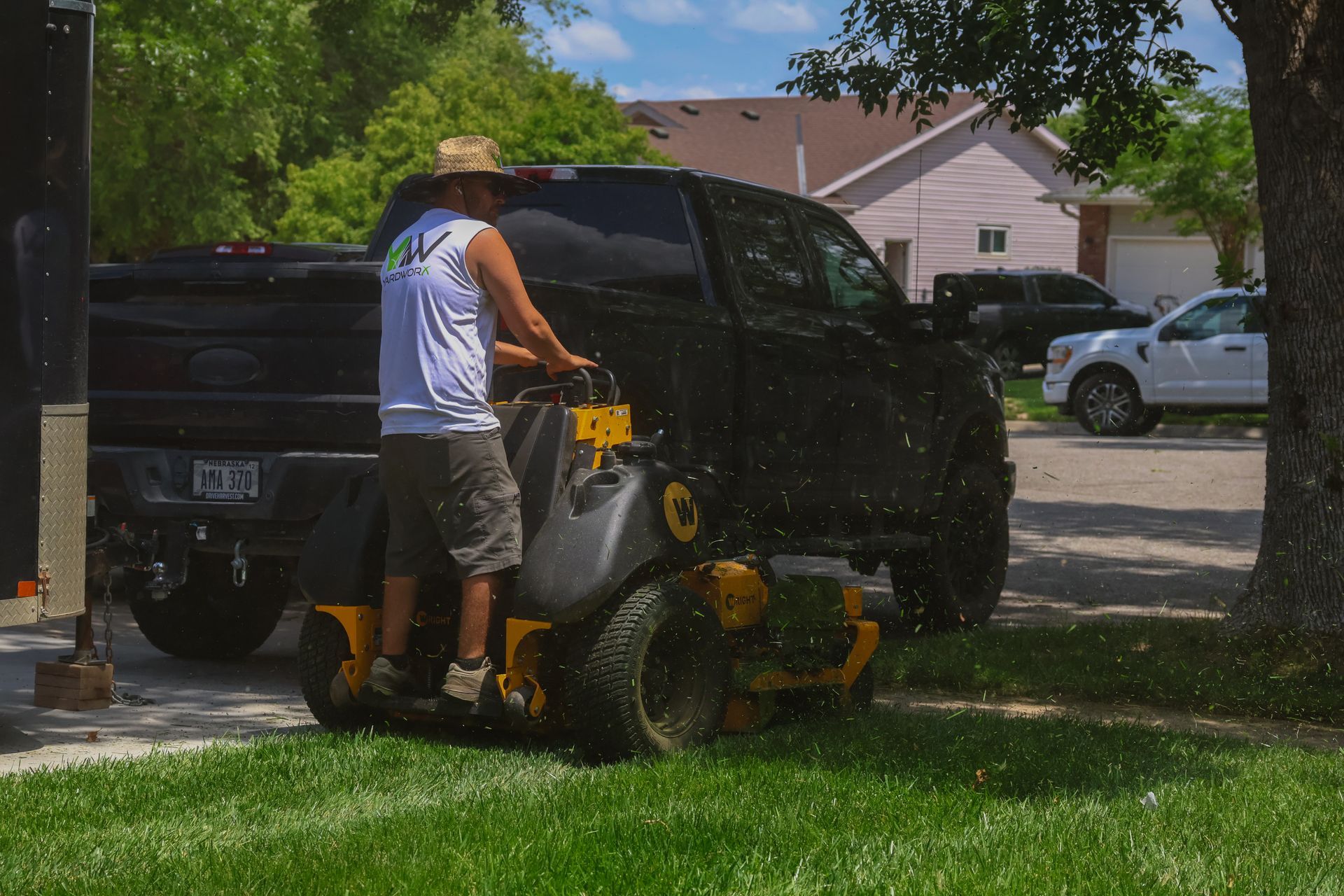 Man mowing lawn with a riding mower next to a black pickup truck.