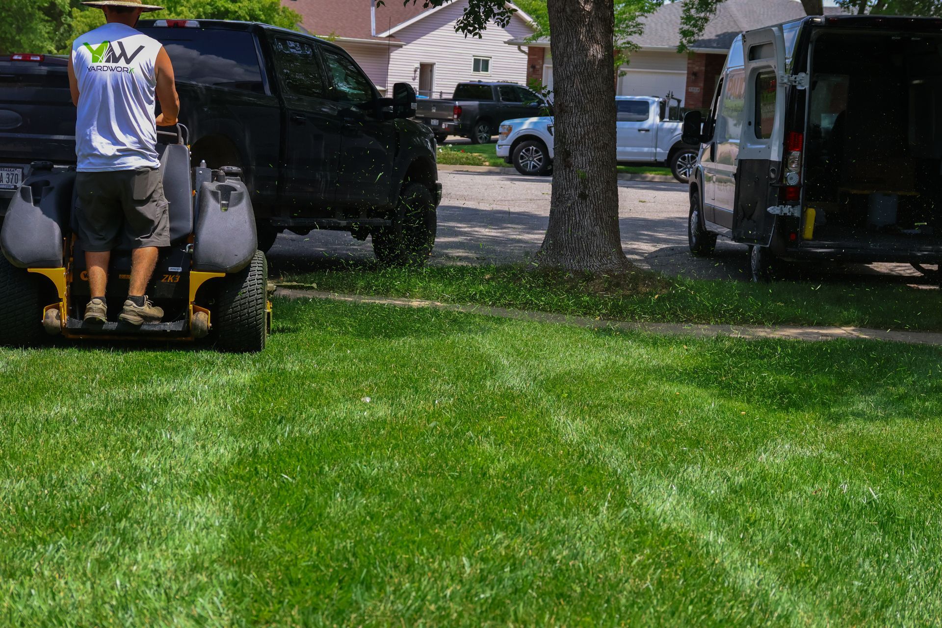 Man on a lawn care machine spraying a lawn. Truck and van parked nearby.