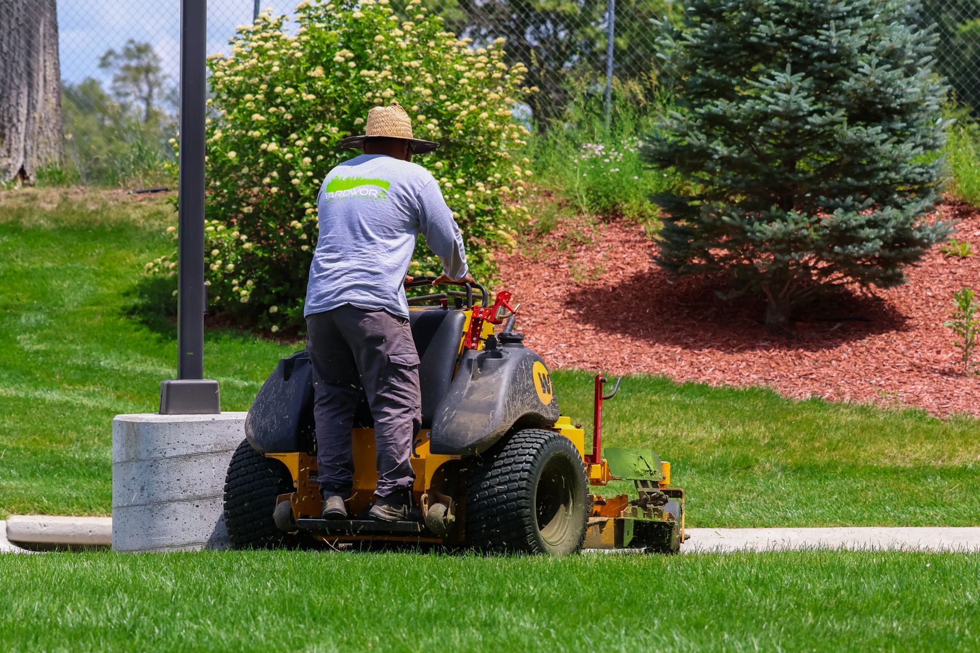 Man mowing grass with a yellow riding lawnmower on a sunny day.