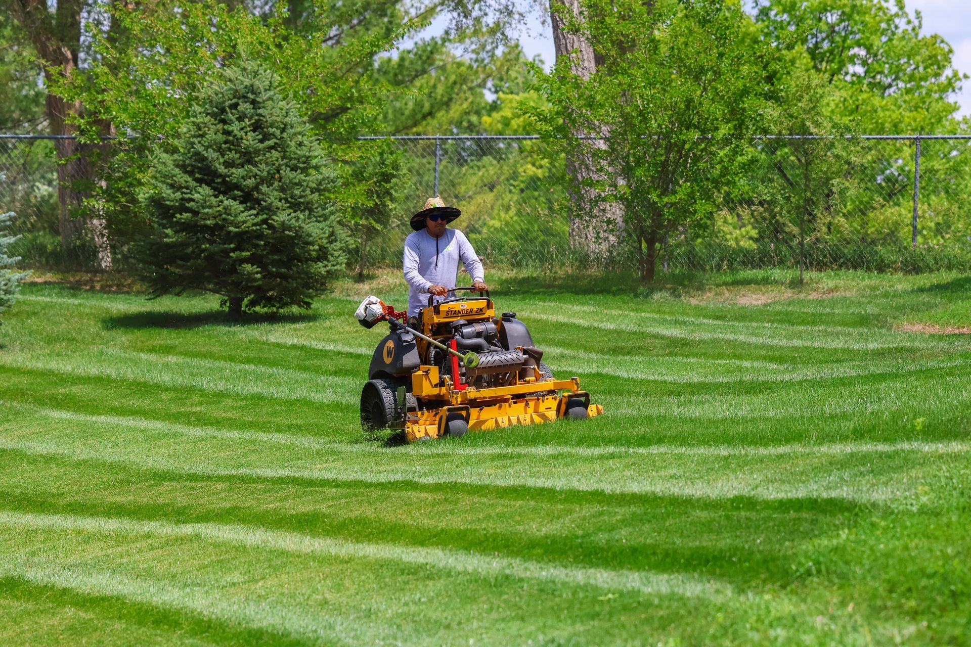 Person mowing lawn with a yellow riding mower, creating striped patterns in the green grass, outdoors.