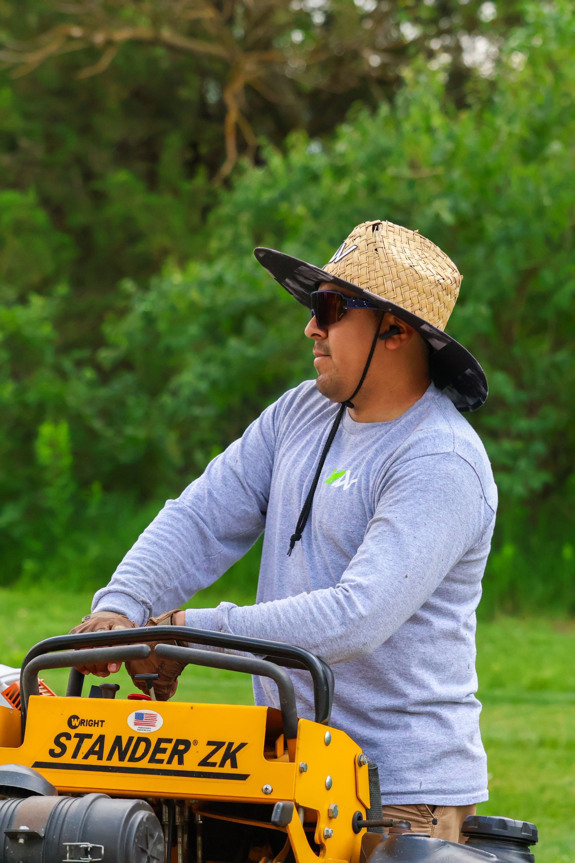 Man operating yellow Stander ZK machine outdoors, wearing a straw hat and long-sleeve shirt.