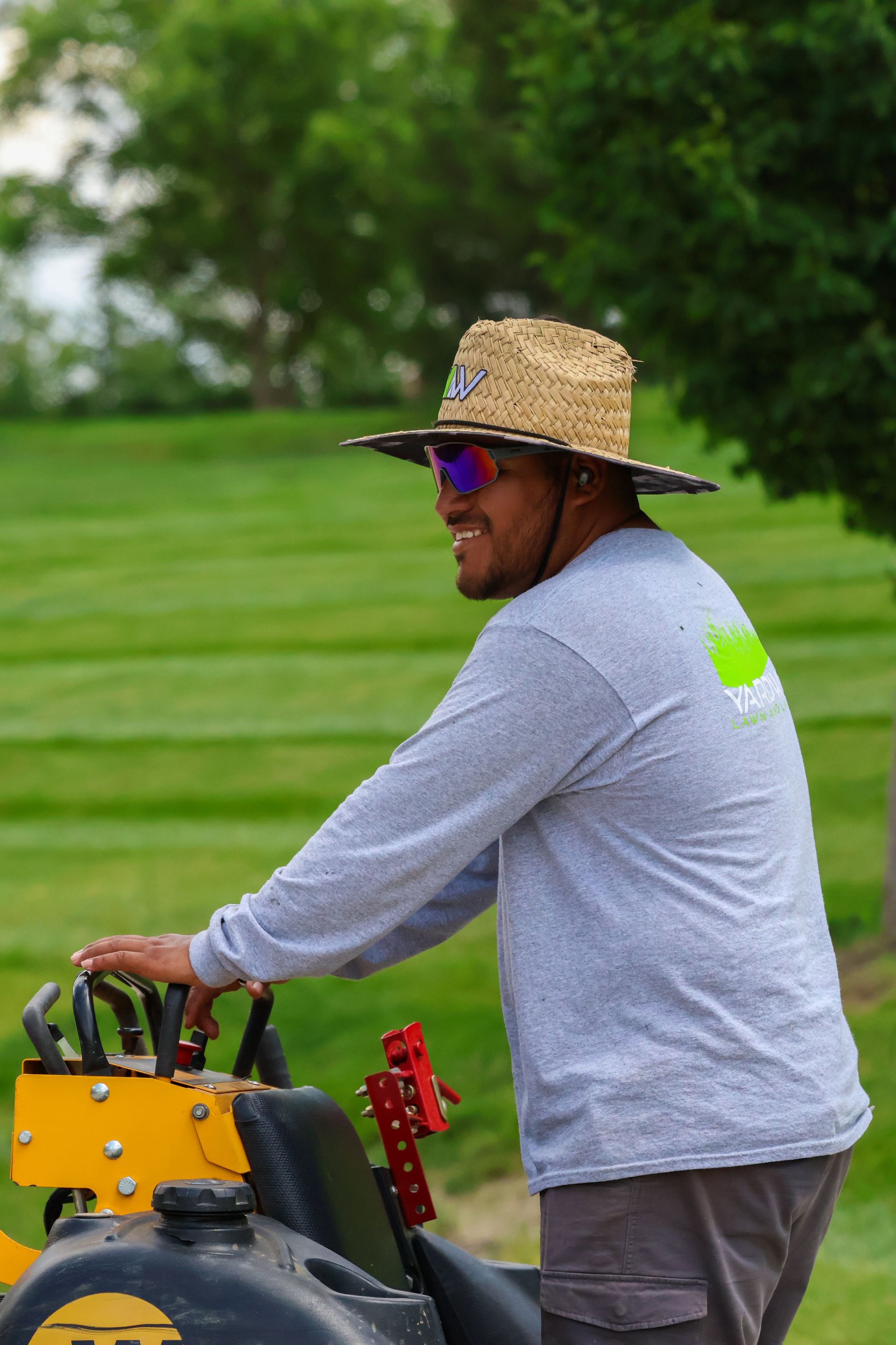 Person in straw hat and sunglasses operating a lawn mower on a green lawn.