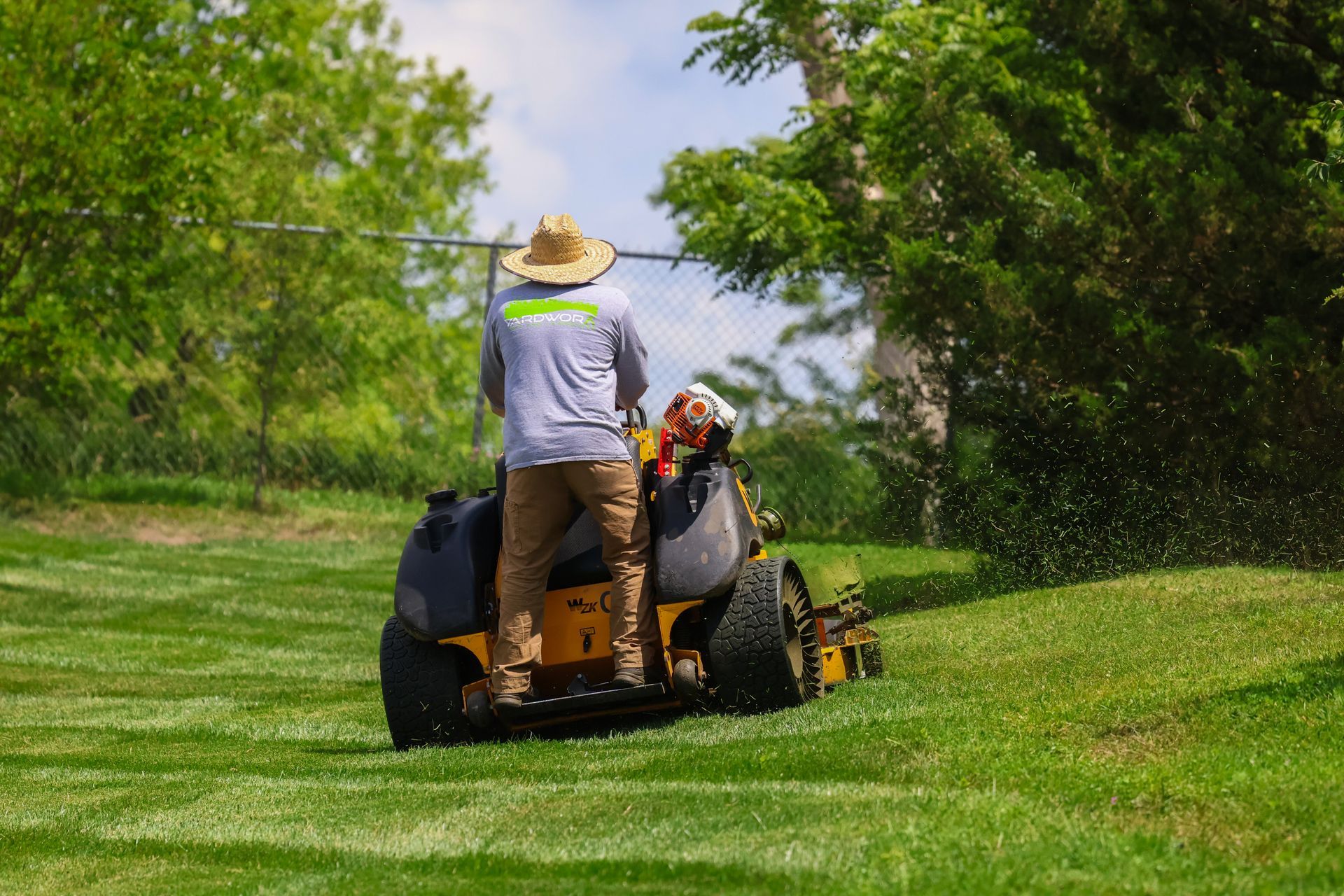 A person mowing a grassy hill with a riding lawn mower.