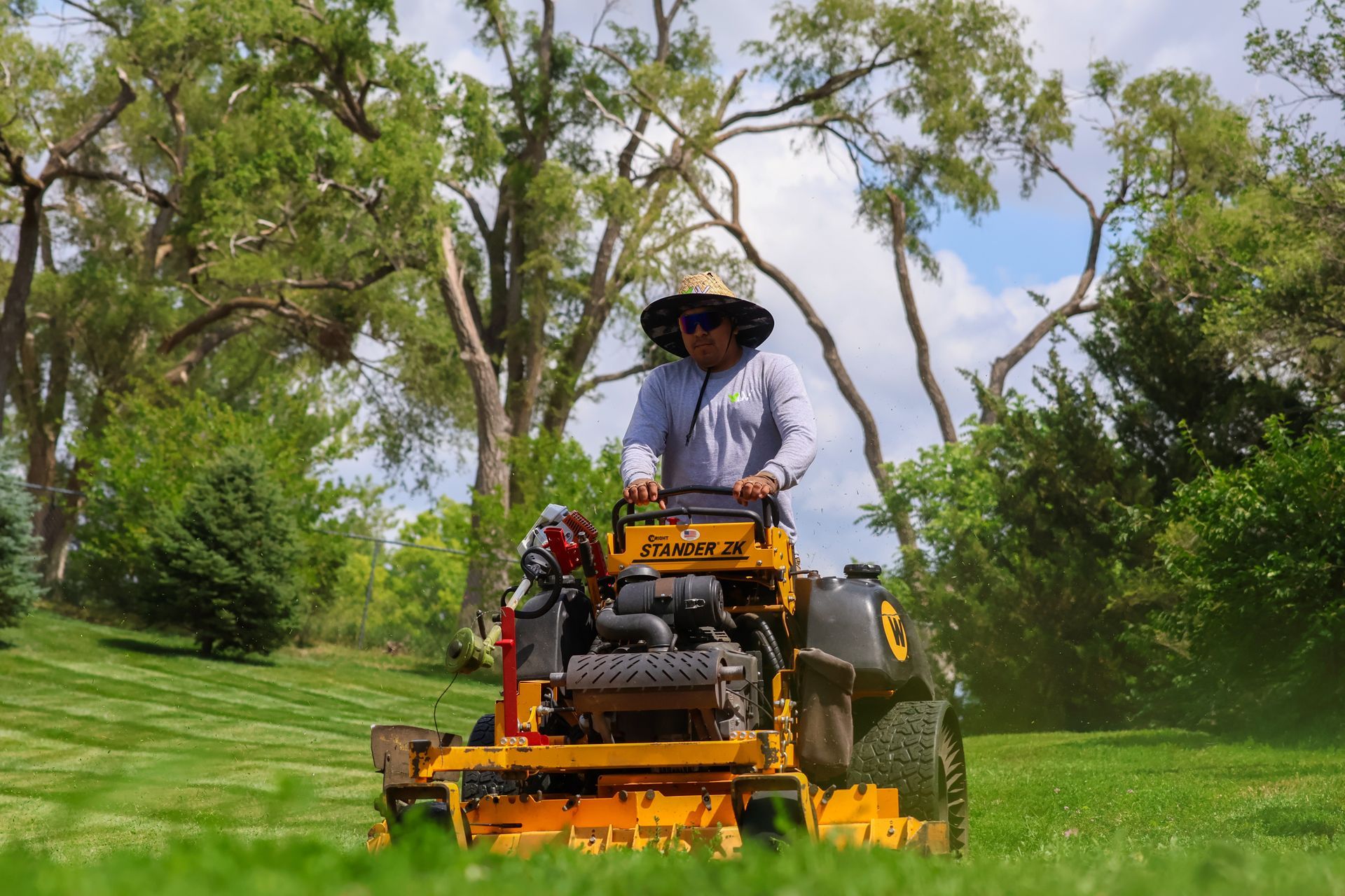 Person mowing lawn with a yellow riding mower on a sunny day.