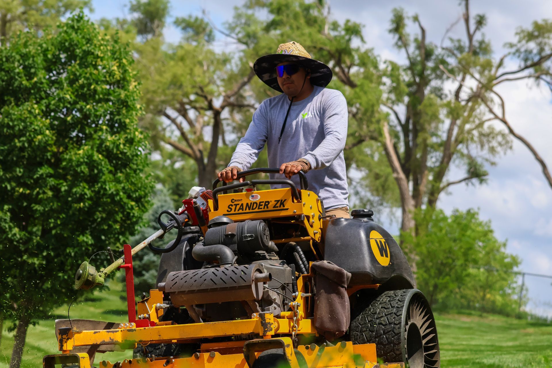 Man operating a yellow lawnmower on a green lawn, wearing a hat and light-colored long-sleeved shirt, sunny day.