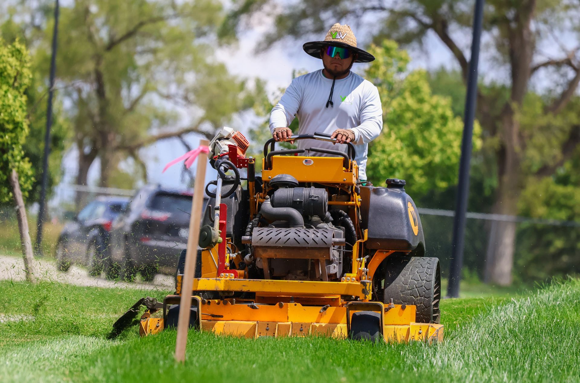 Person mowing grass with yellow riding mower on a sunny day.