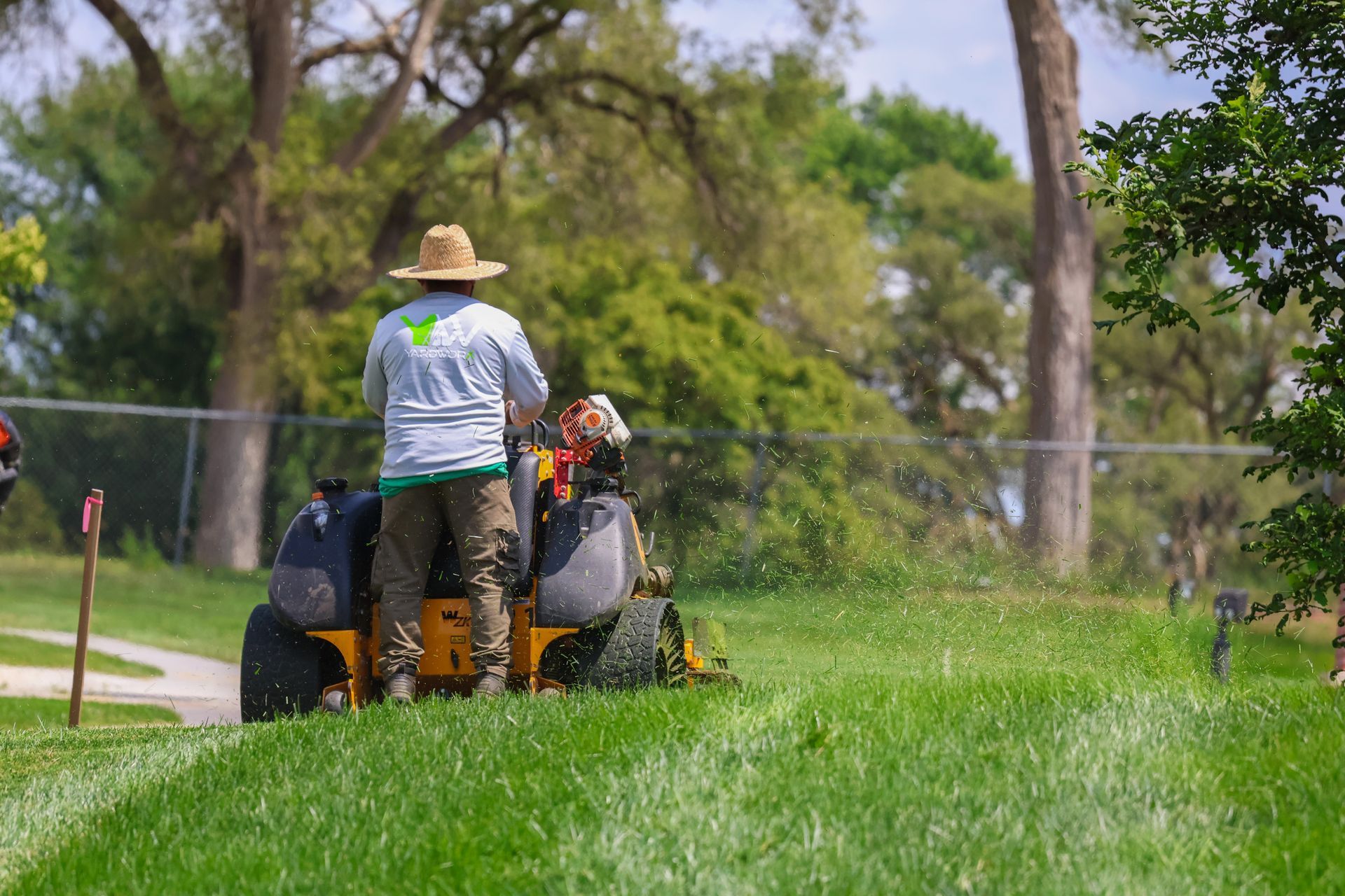 Person mowing grass on a riding lawnmower in a grassy area with trees in the background.