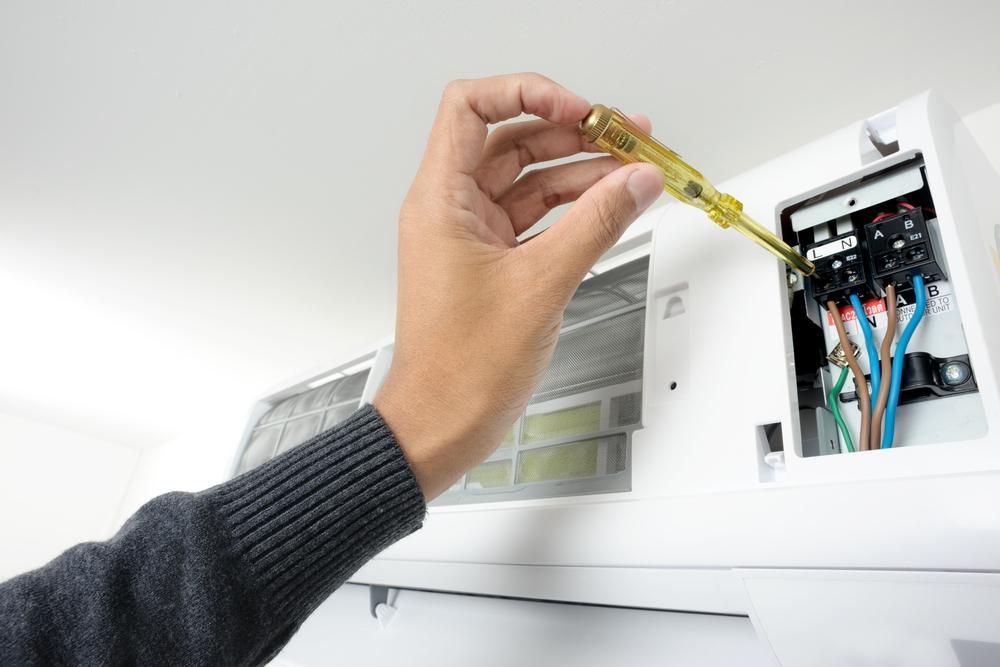A Person is Fixing an Air Conditioner With a Screwdriver — AJM's Air Conditioning Centre in Coraki, NSW