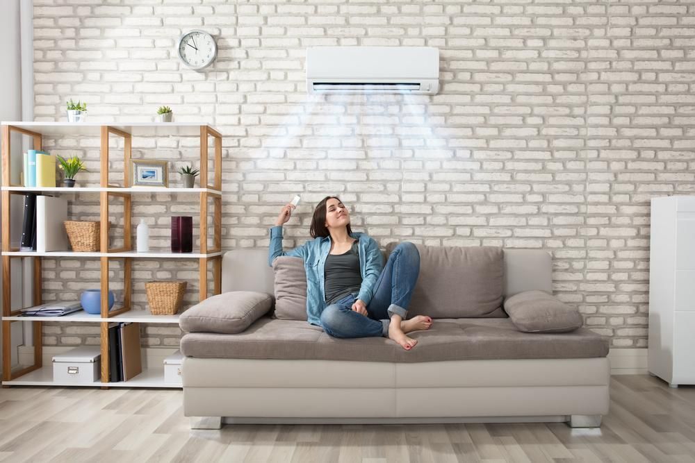 A Woman is Sitting on a Couch Under an Air Conditioner in a Living Room — AJM's Air Conditioning Centre in Lismore, NSW