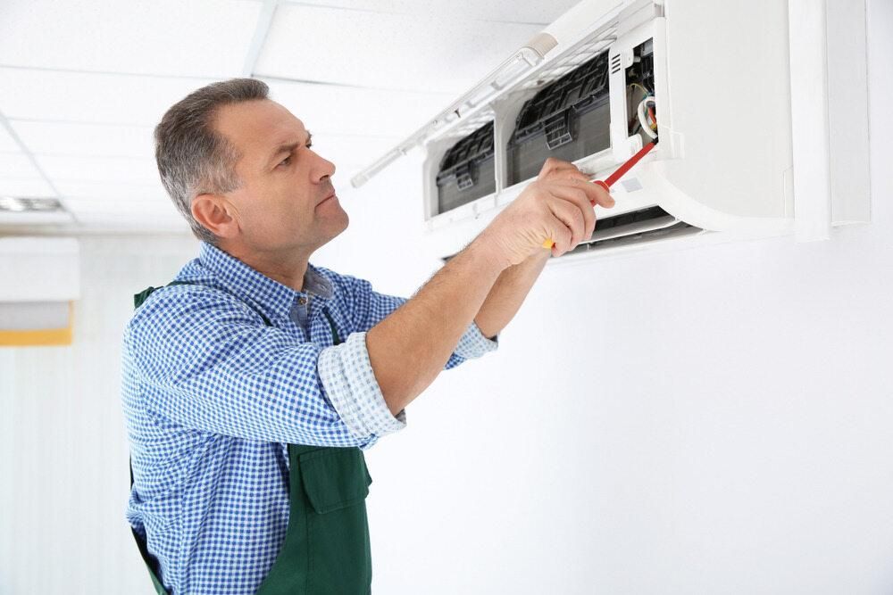 A Man is Fixing an Air Conditioner With a Screwdriver — AJM's Air Conditioning Centre in Woodburn, NSW