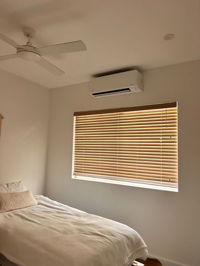 A White Air Conditioner is sitting above some curtains in a white bedroom — AJM's Air Conditioning Centre in Lismore, NSW