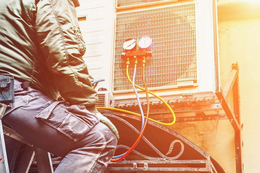 A Man is Sitting on a Ladder Working on an Air Conditioner — AJM's Air Conditioning Centre in Lismore, NSW