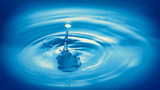 Blue water droplet splash creating ripples on a glossy blue surface