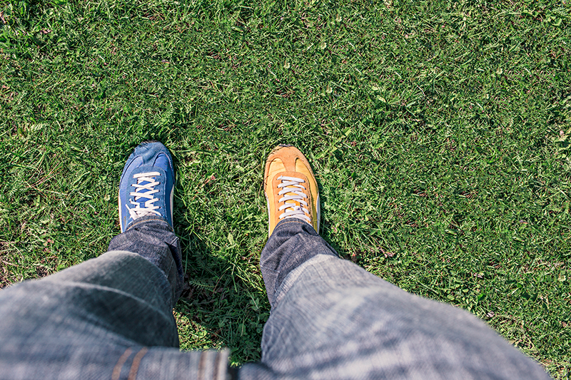 Person standing on grass wearing mismatched blue and orange sneakers and jeans
