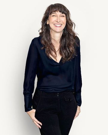 Smiling woman in a black blouse and pants standing against a beige background