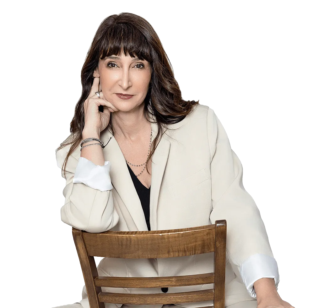 Woman standing against a white background, wearing a dark blouse and black pants.