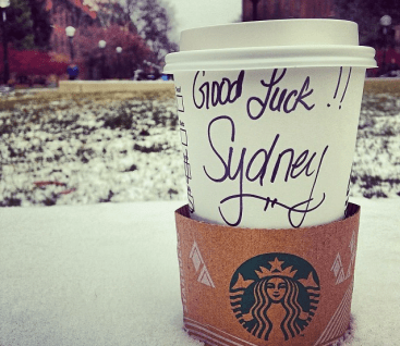 Starbucks cup with handwritten “Good luck!! Sydney!” on a snowy outdoor table