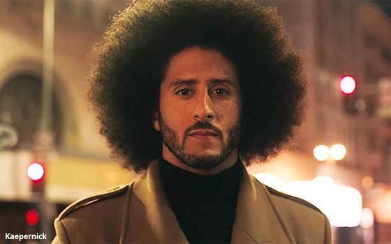 Man with an afro and brown coat standing outdoors at night with blurred city lights behind him
