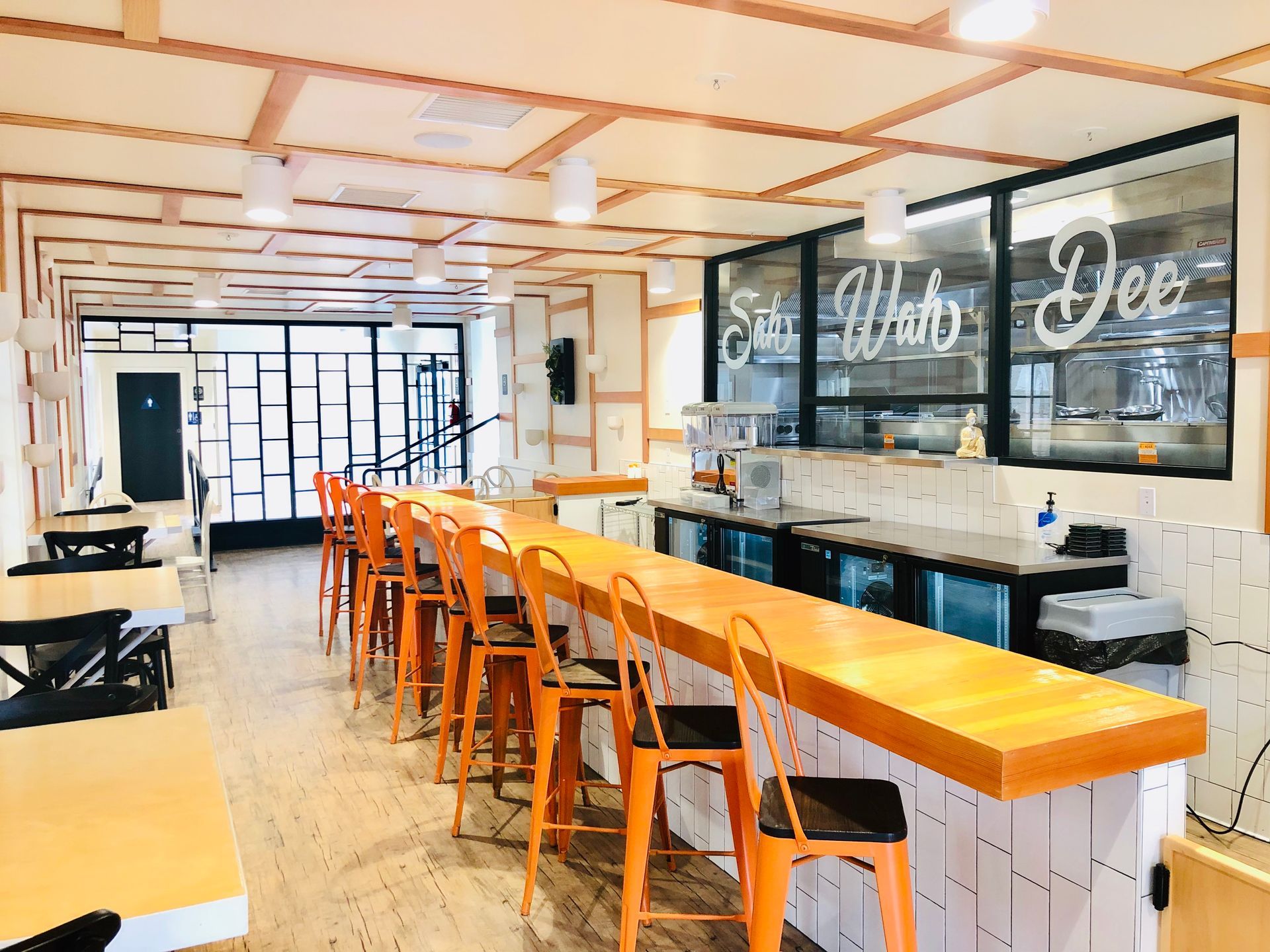 Bright modern cafe interior with orange stools at a long counter and black-framed windows