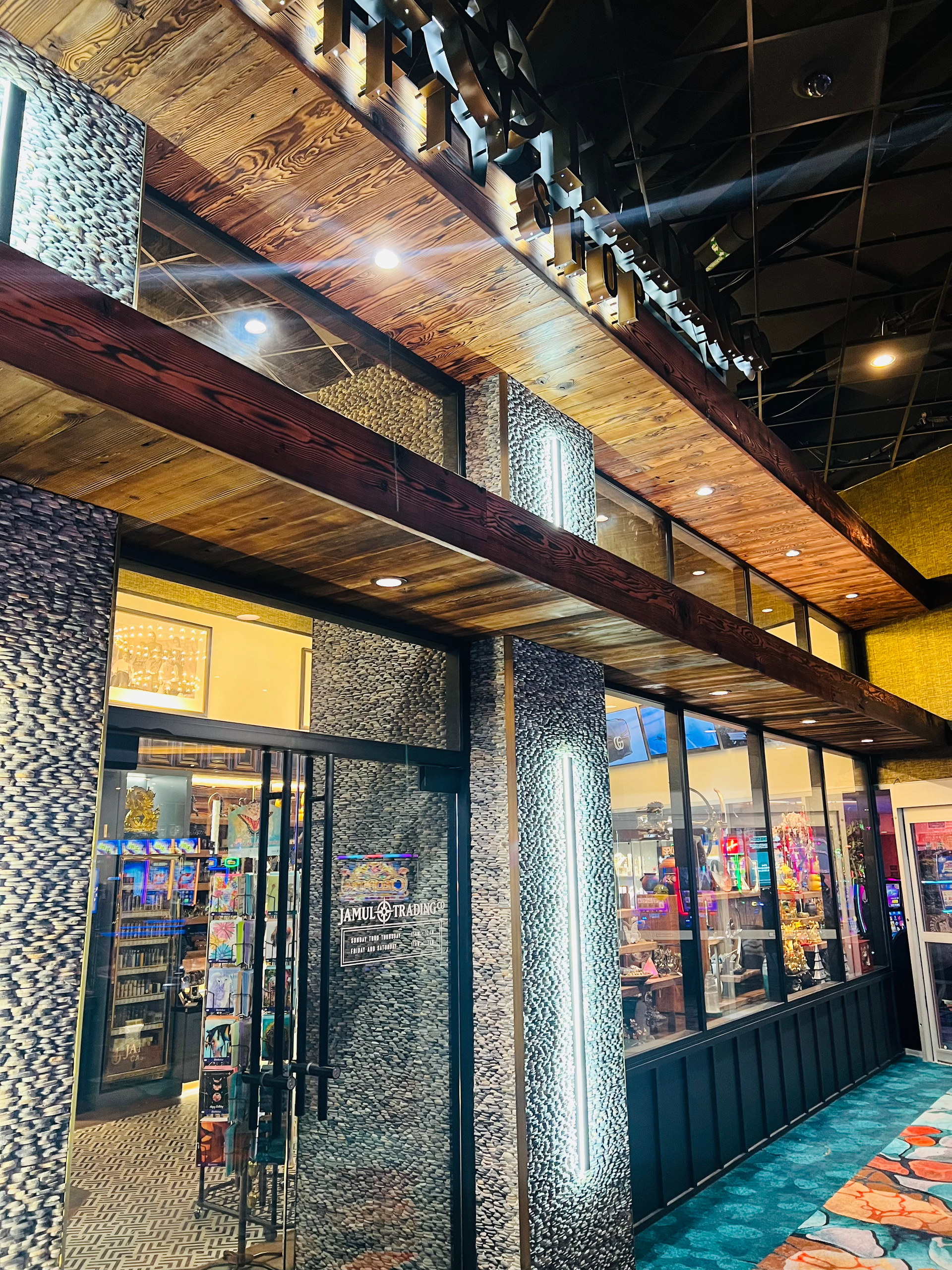 A brightly lit store with glass displays, mosaic-patterned columns, and a long wooden overhang.