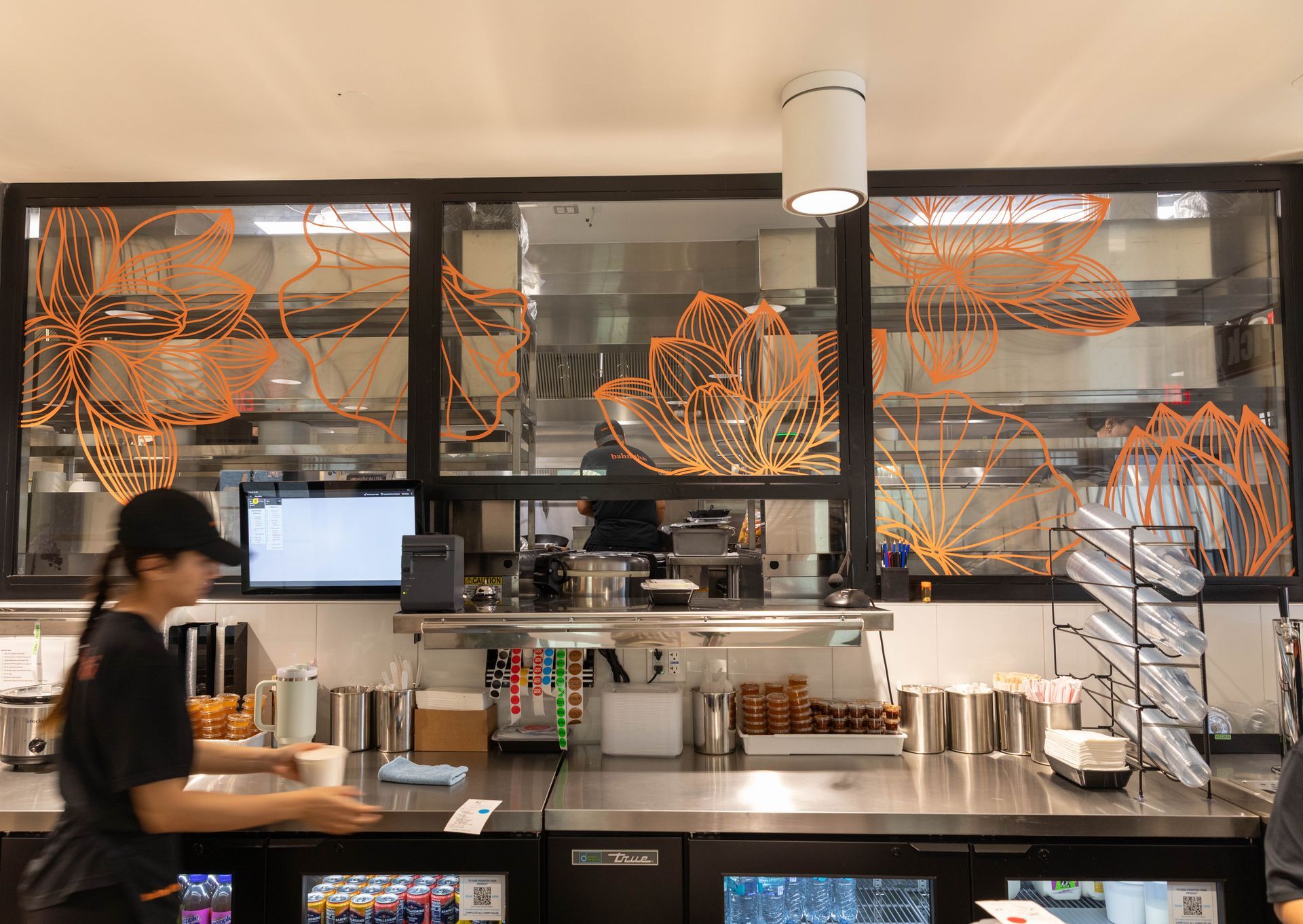 Coffee shop counter with employee and glass menu panels featuring orange leaf designs