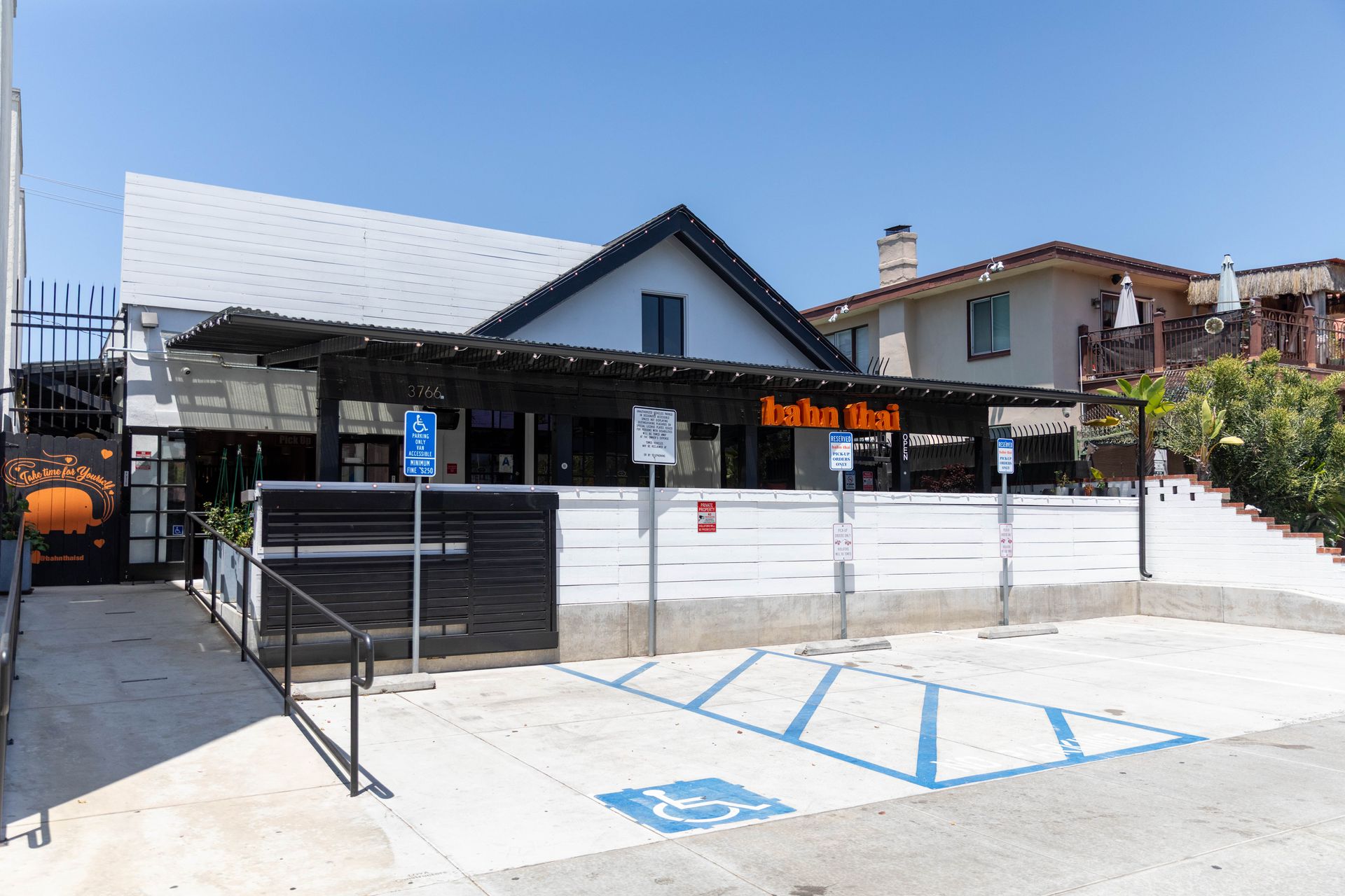 Small black restaurant with white walls and orange sign, viewed from the parking lot on a sunny day