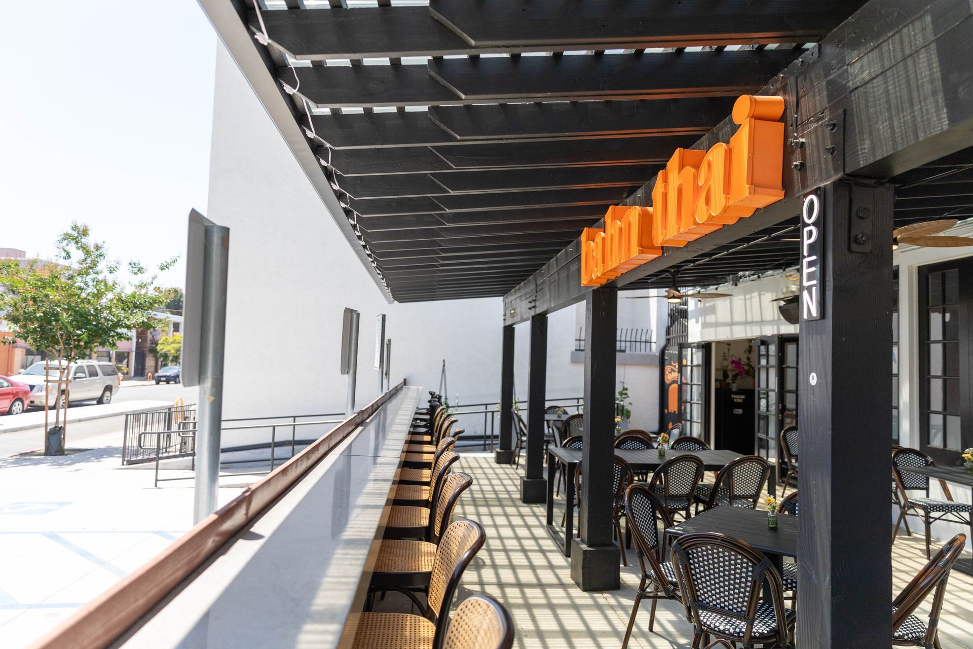 Outdoor café patio with black awning, orange sign, and rows of tables and chairs along a sidewalk