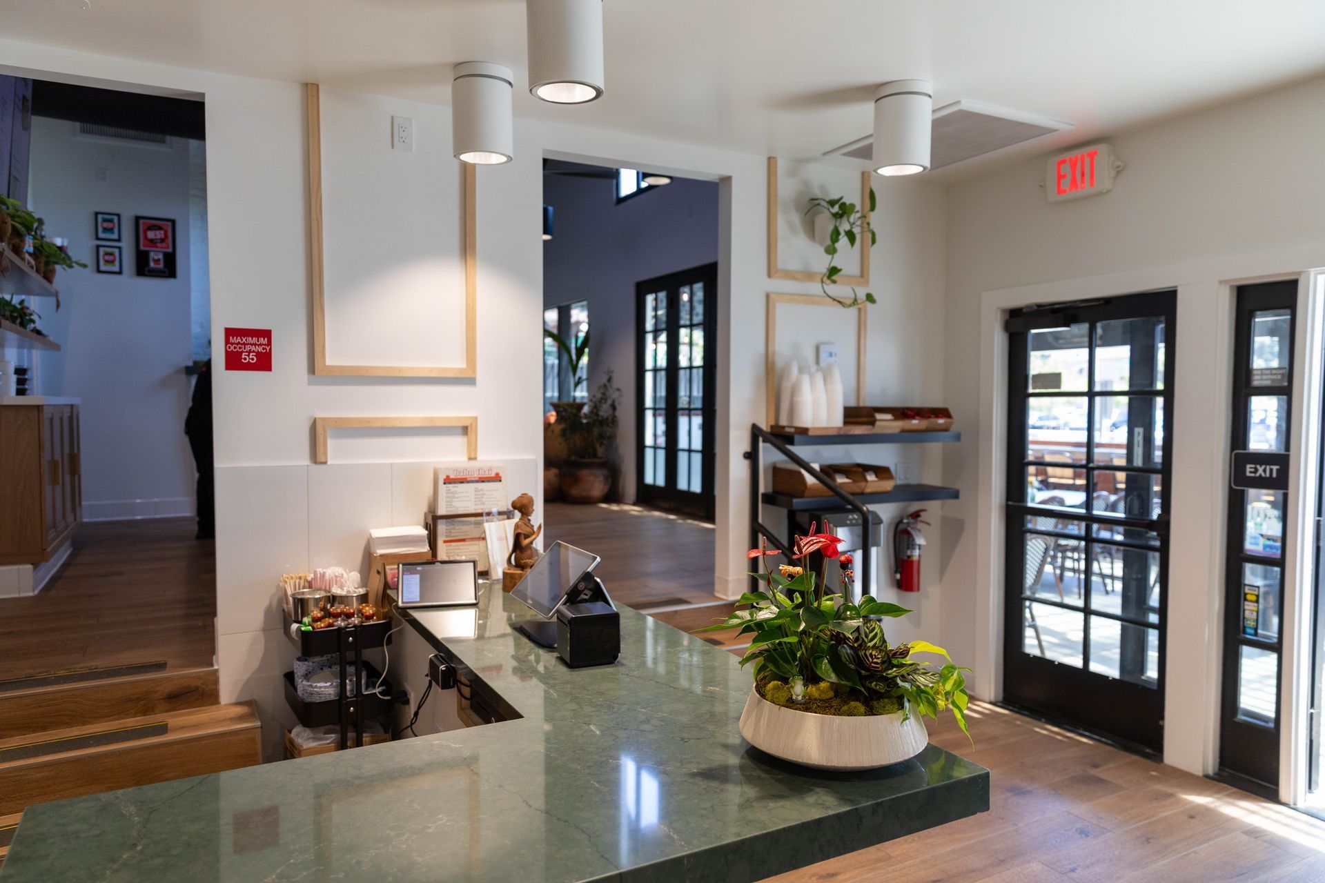 Bright café interior with glass counter, potted plant, and black-framed doors by the entrance