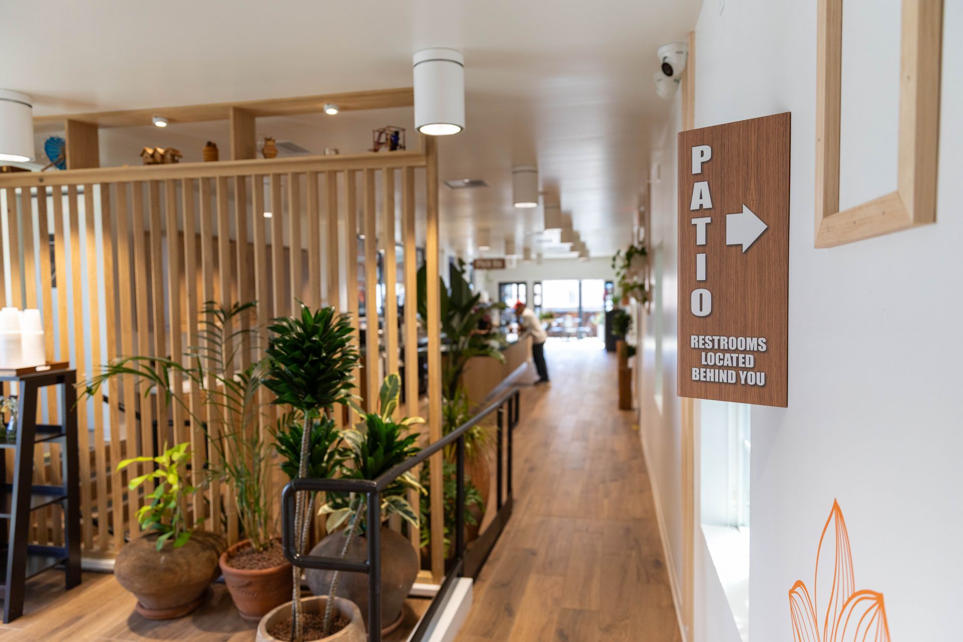 Bright café corridor with wooden decor, plants, and a sign pointing to the patio.
