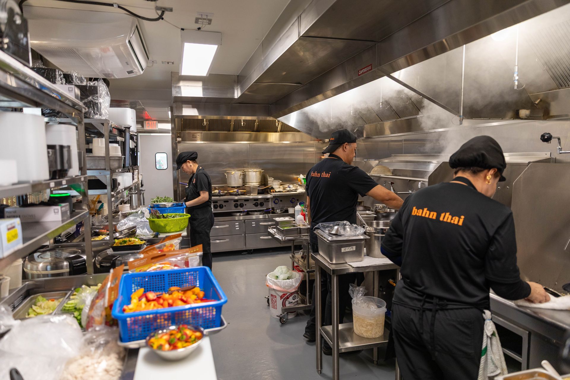 Chefs working in a busy stainless-steel restaurant kitchen with trays of prepared food