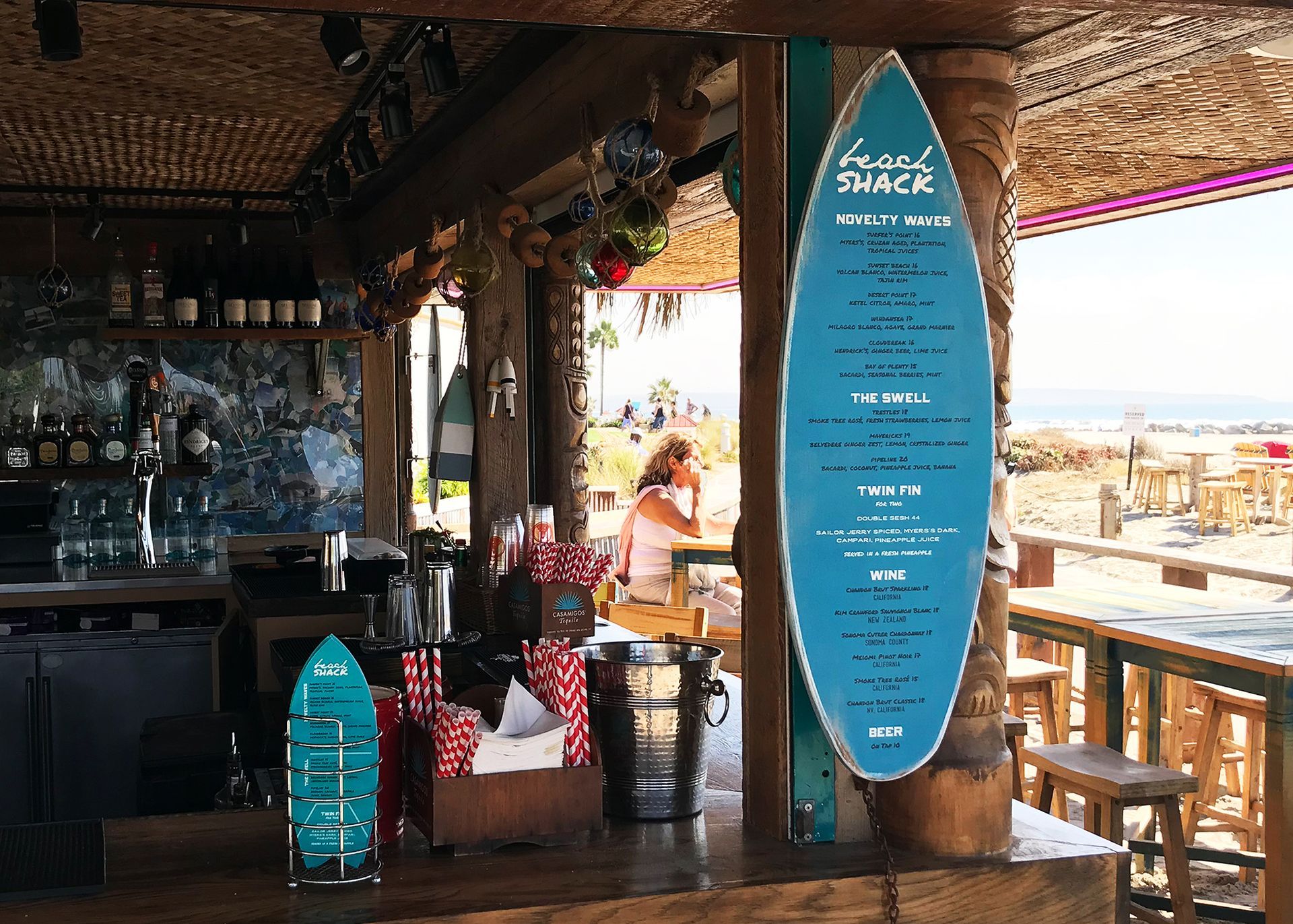 Beach bar with blue surfboard menu sign, tables, stools, and ocean view