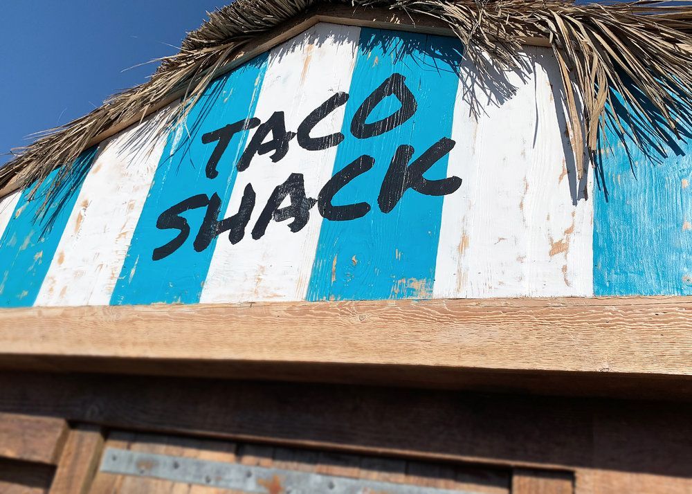 Taco Shack sign on a blue-and-white striped rooftop under thatch trim