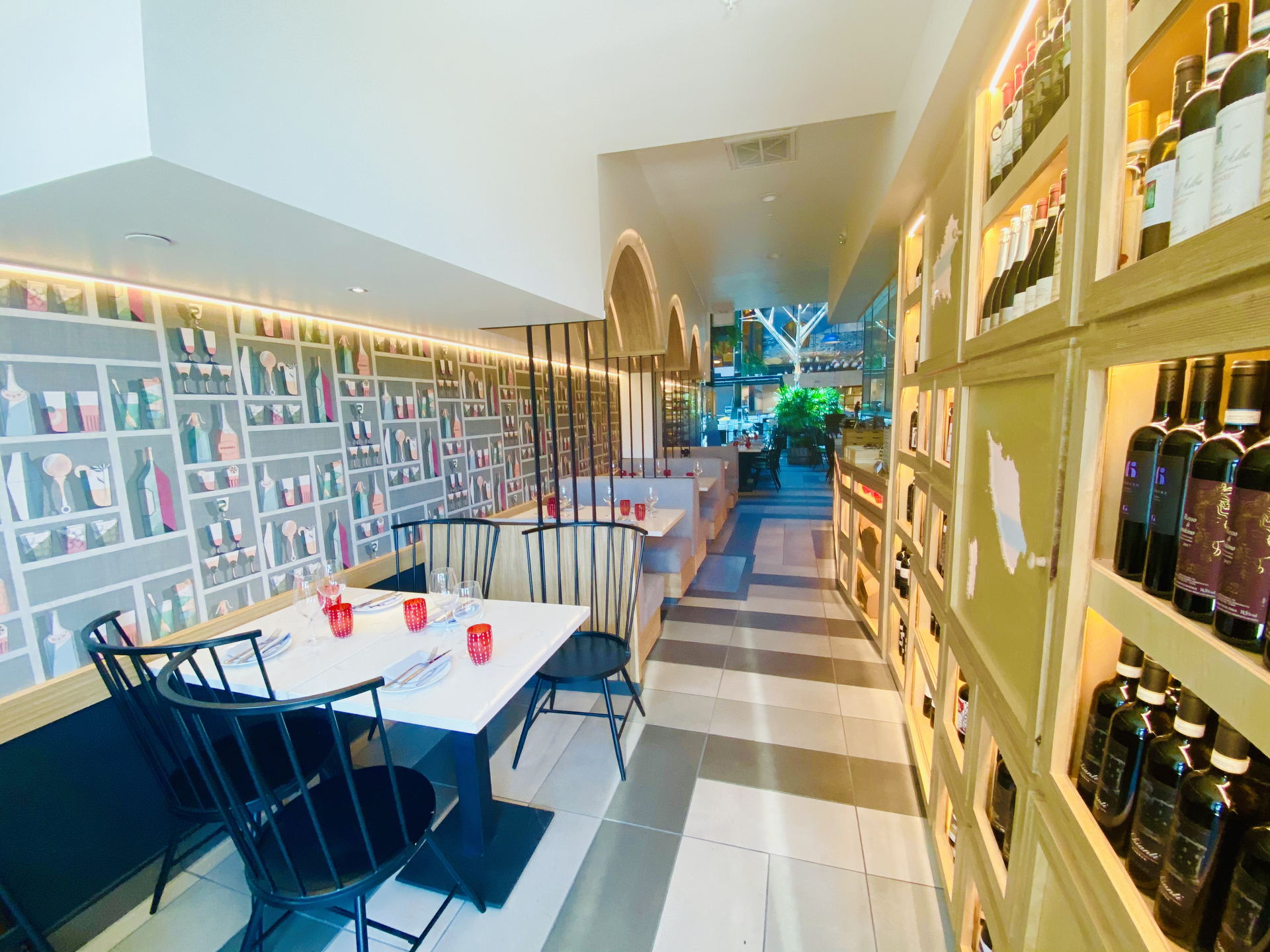 Bright café interior with white tables, blue chairs, striped floor, and wall shelves of bottles and decor